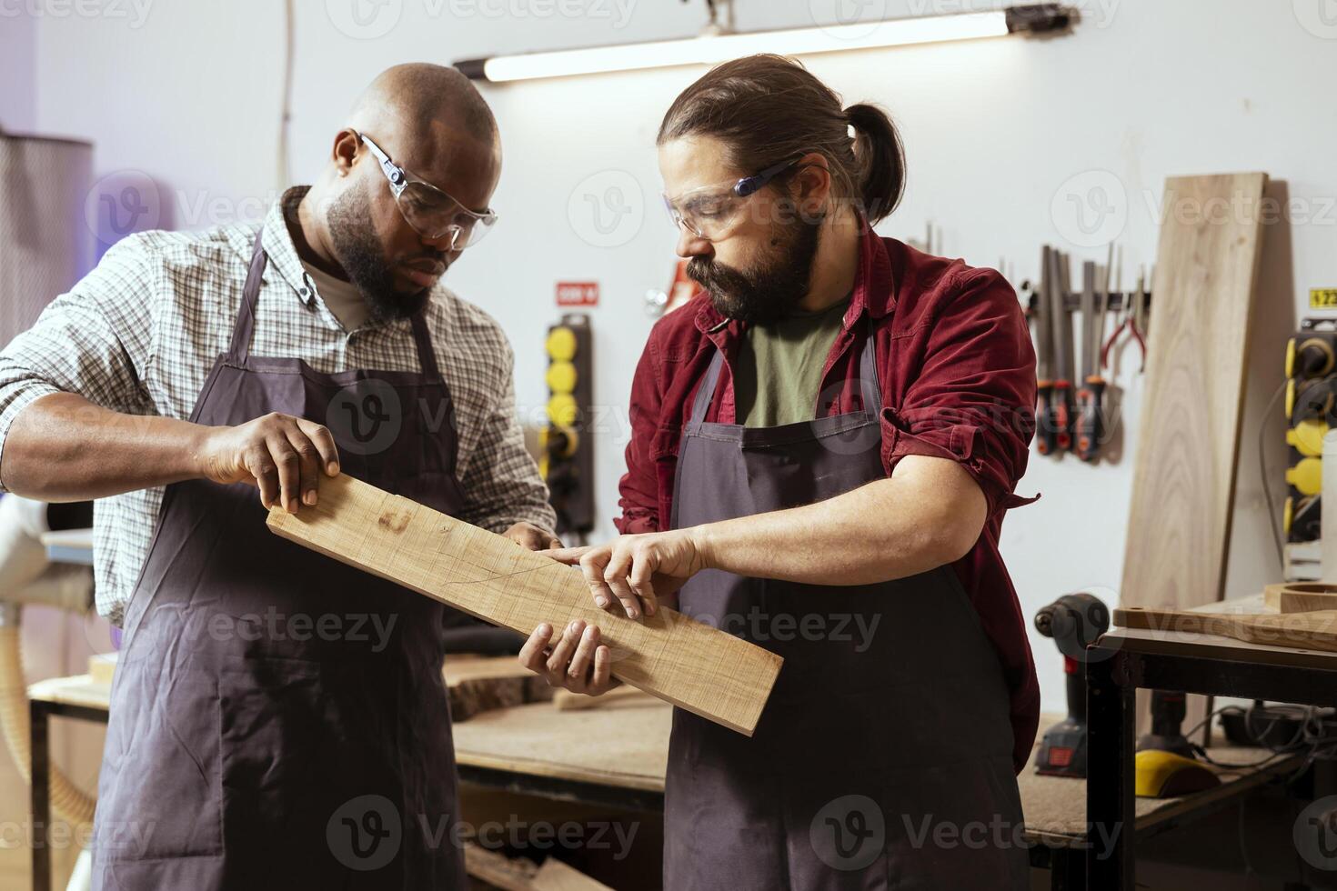 Manufacturer and apprentice wearing safety glasses selecting high quality wood materials. Cabinetmaker and colleague using protective equipment doing quality assurance on lumber piece photo
