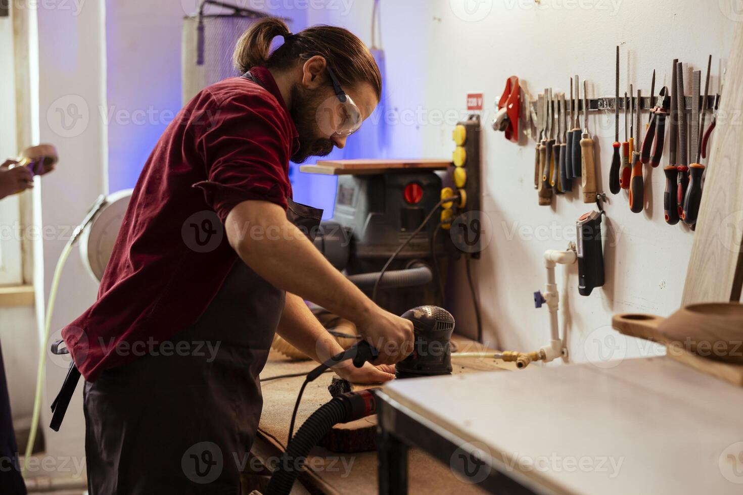 Carpenter using angle grinder on timber block to smooth surfaces by abrasion with sandpaper. Woodworking professional using orbital sander equipment for furniture assembling job in studio photo