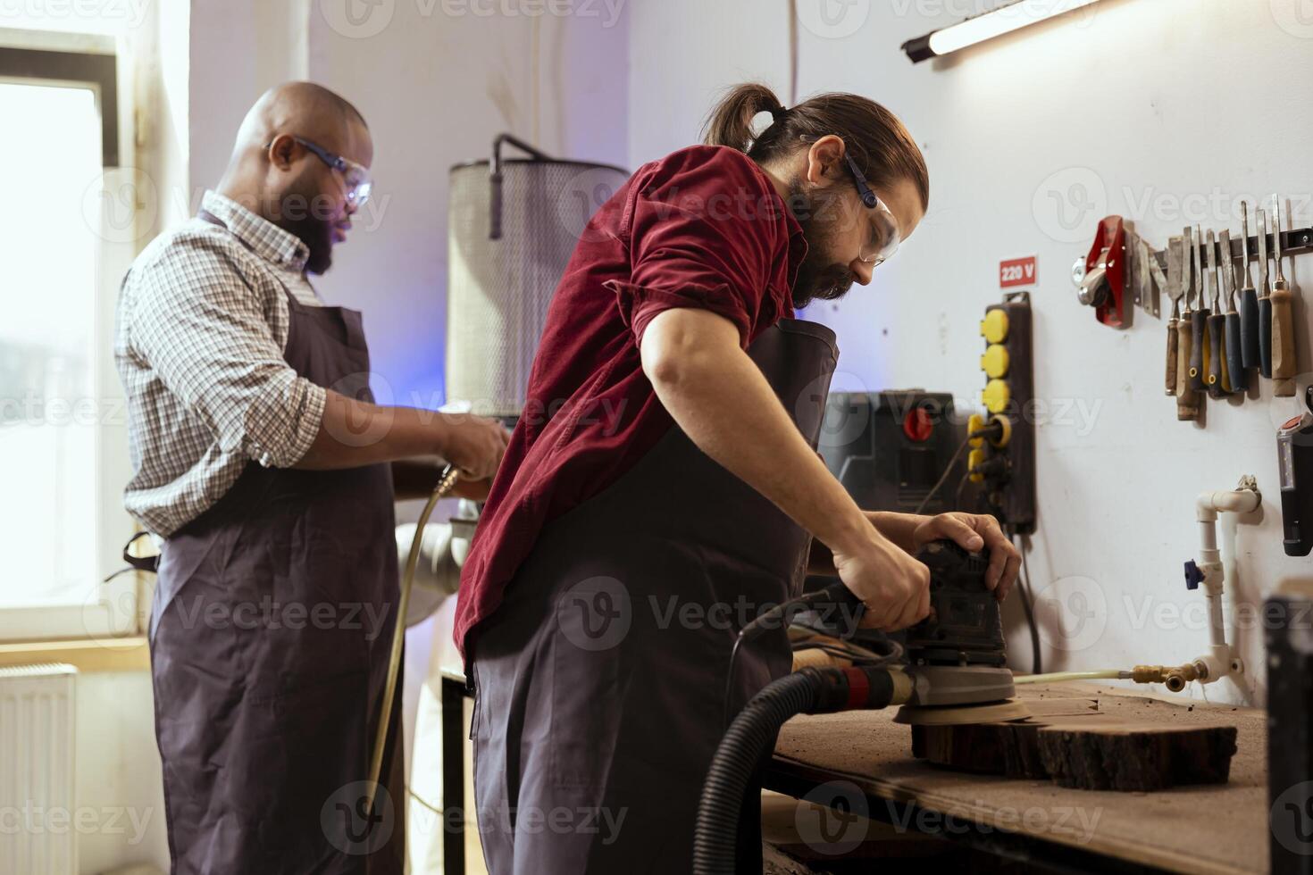 Carpenter collaborating with african american apprentice using orbital sander with fine sandpaper to achieve refined finish. Man and coworker using angle grinder on wood block for professional results photo