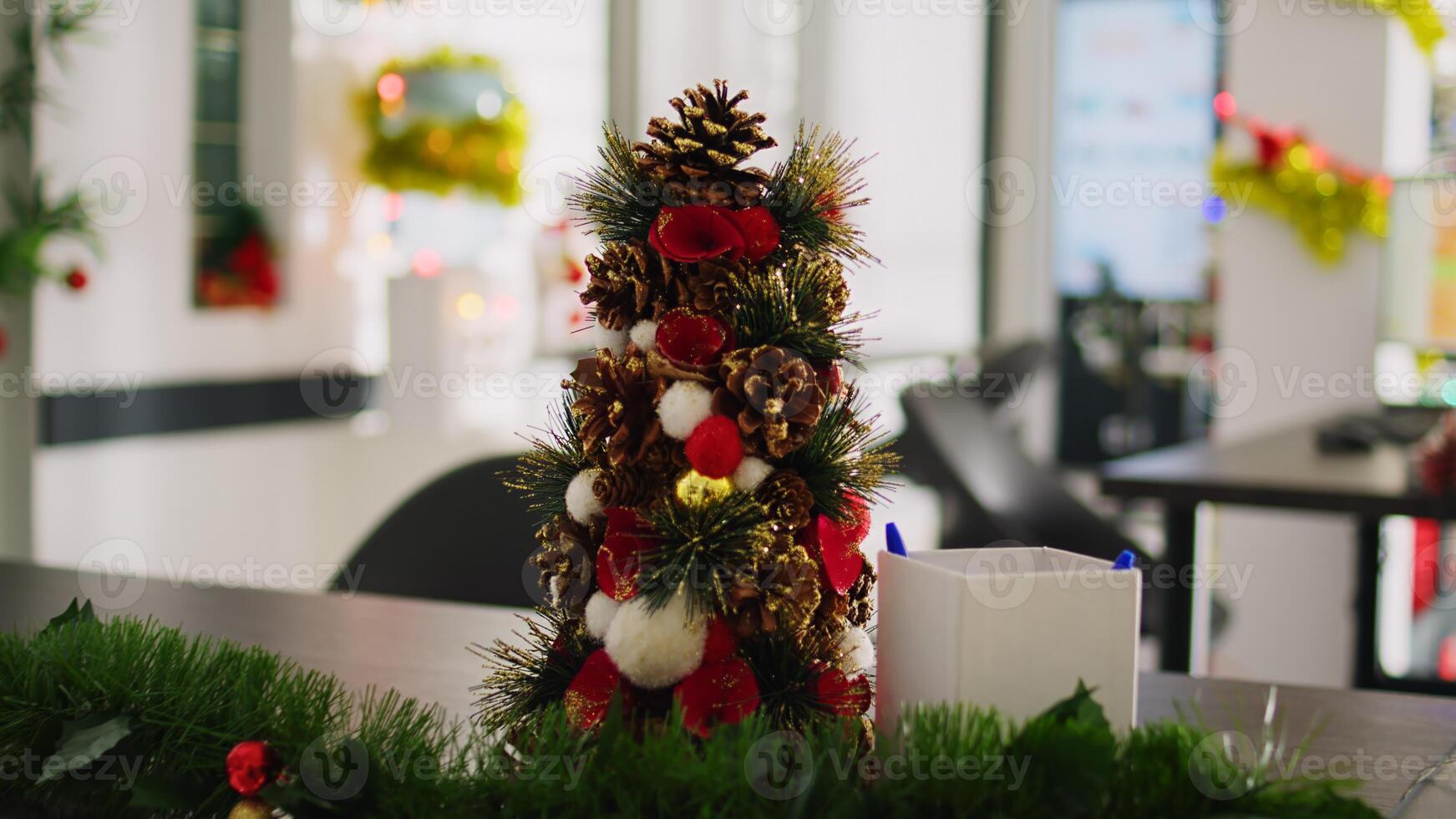Dolly in close up shot on mini Christmas pine tree decoration placed in empty office. Festive workplace filled with xmas lights, garlands and wreaths during winter holiday season photo