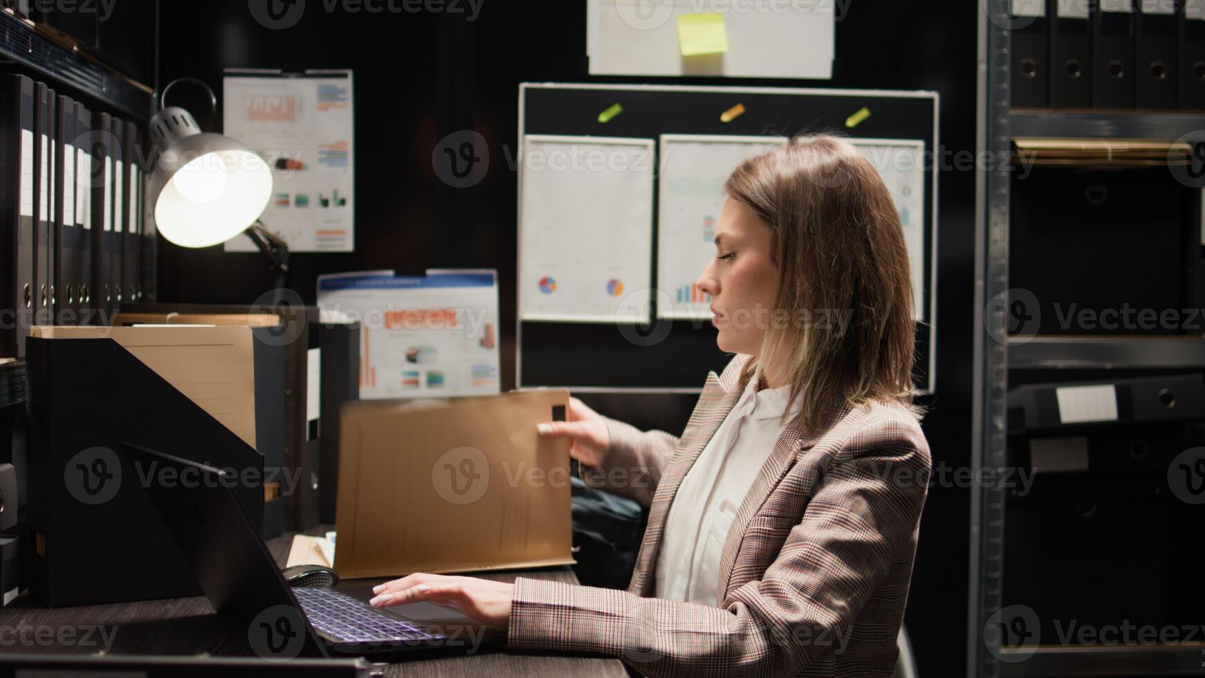 Close-up of caucasian female detective closing laptop and folder, leaving her workstation. After obtaining information to solve criminal investigation, policewoman stands and exits the evidence room. photo
