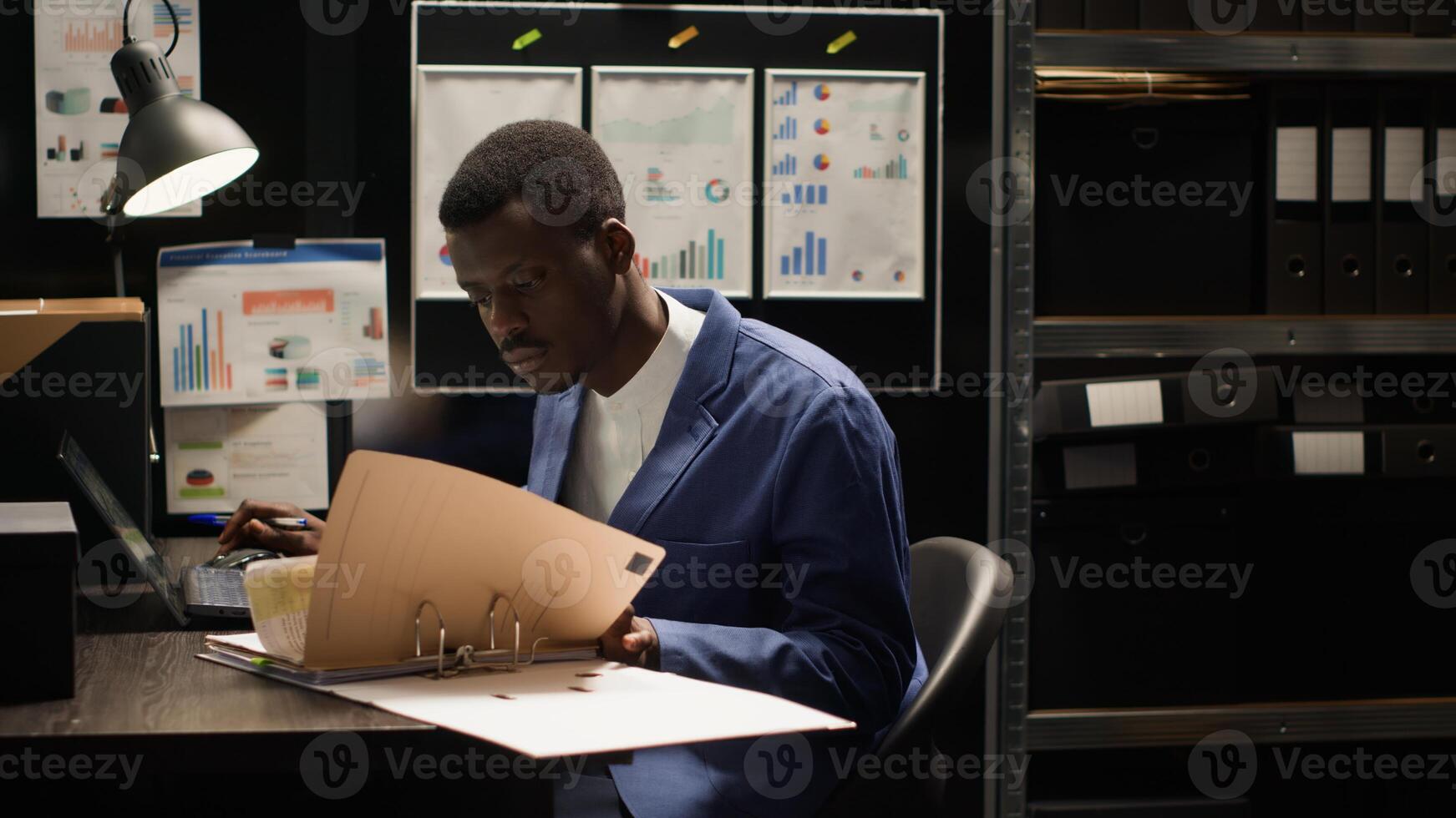 Diligent private investigator grabbing files from shelves to conduct thorough investigation. African american agent with laptop and research papers, analyzes evidence and gathers information. photo
