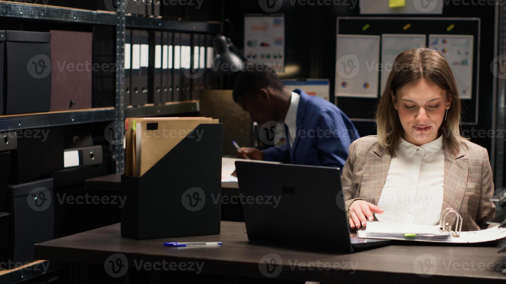 Caucasian policewoman examines case files and discusses information with african american policeman in evidence room. Multiethinc private investigators talking about solving criminal investigation. photo