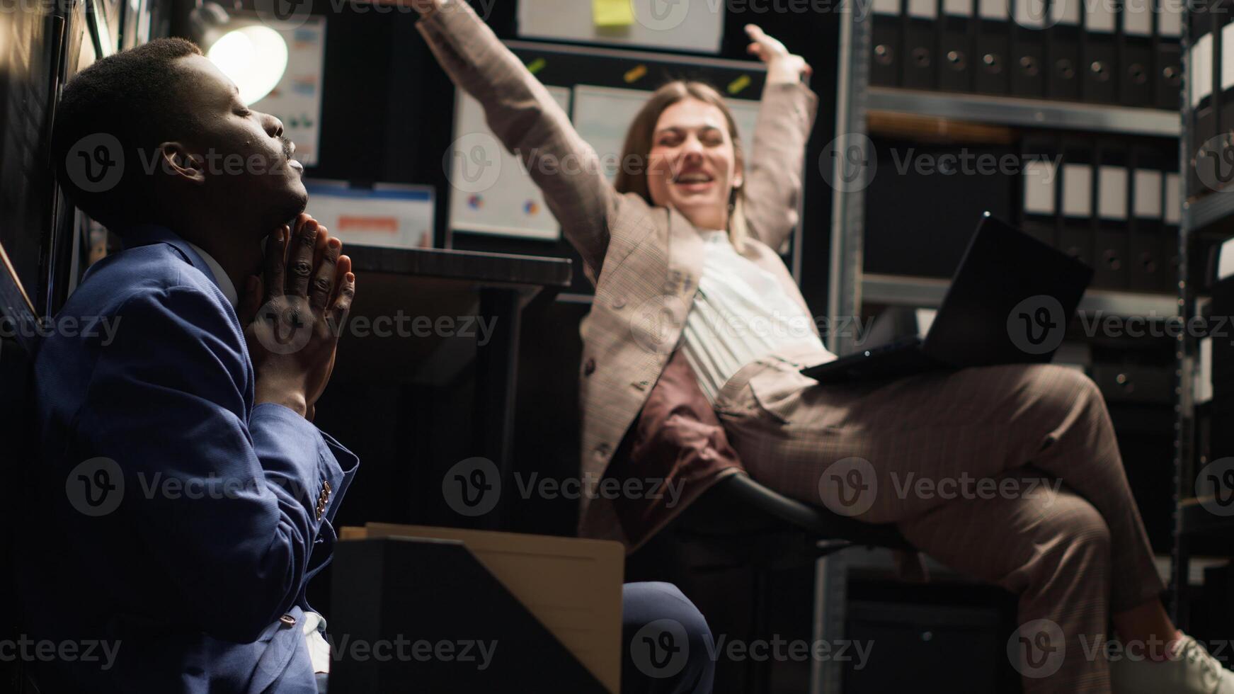Diverse team of exhausted private investigators in incident room analyze evidence, review files, and conduct research to solve case. Two detectives feeling tired about criminal investigation reports. photo