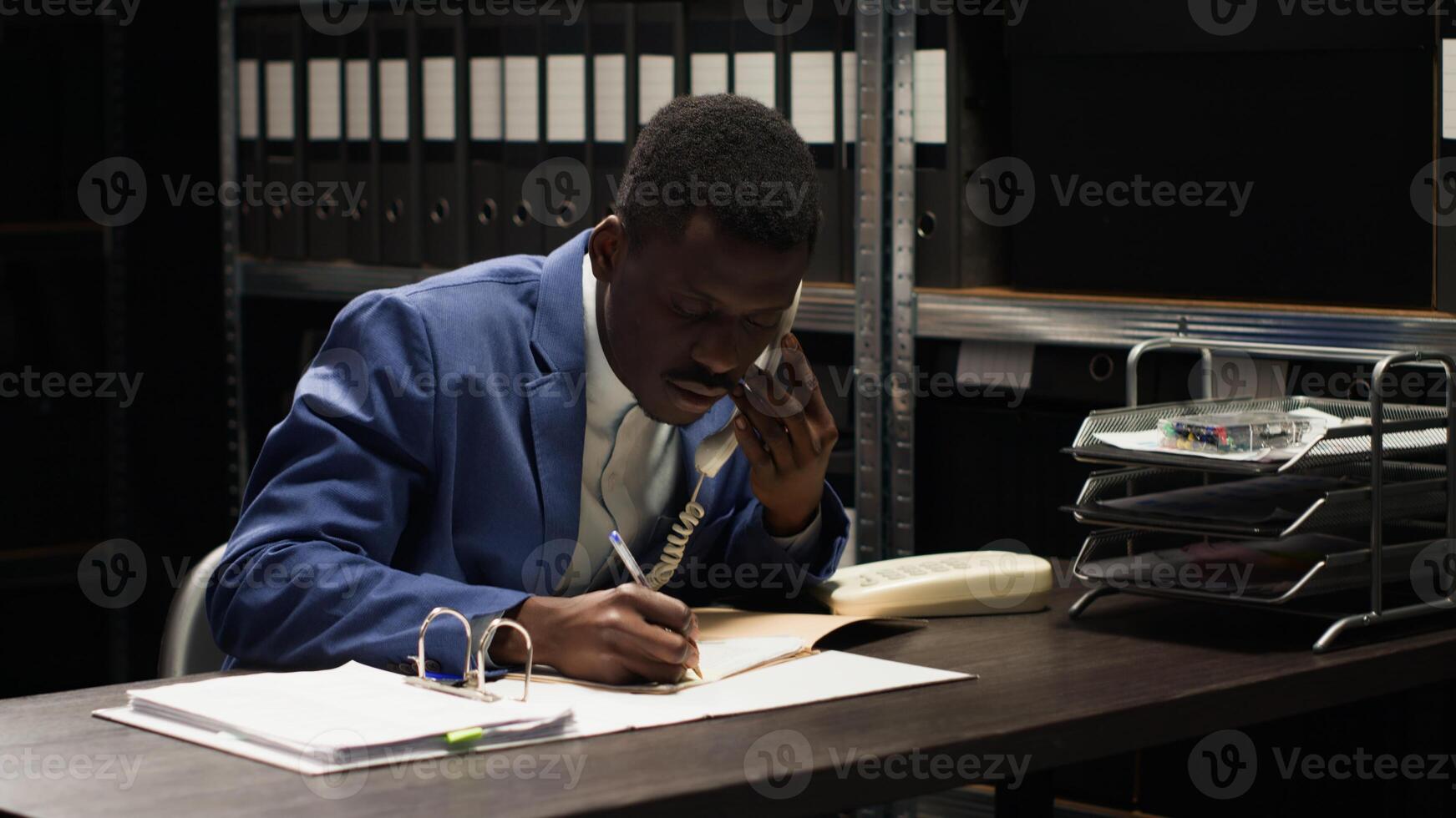 Black policeman conducts confidential investigation, analyzes evidence and makes crucial phone calls. African american law officer uses telephone to collect classifed witness statements and clues. photo