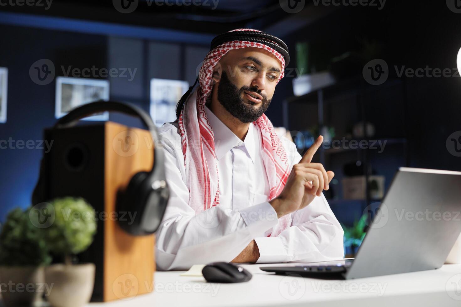 Close-up of an Arabian businessman dressed traditionally working intently at his contemporary desk, utilizing wireless technology and internet connection for research and conferencing. photo