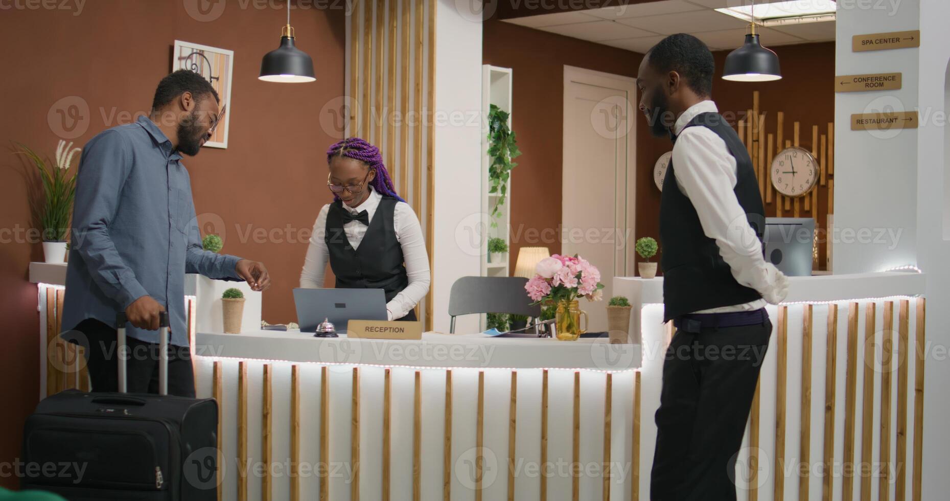 Guest asks for service and room card at front desk, ringing bell to call for staff member at reception. African american traveller with baggage requesting access for hotel room. photo