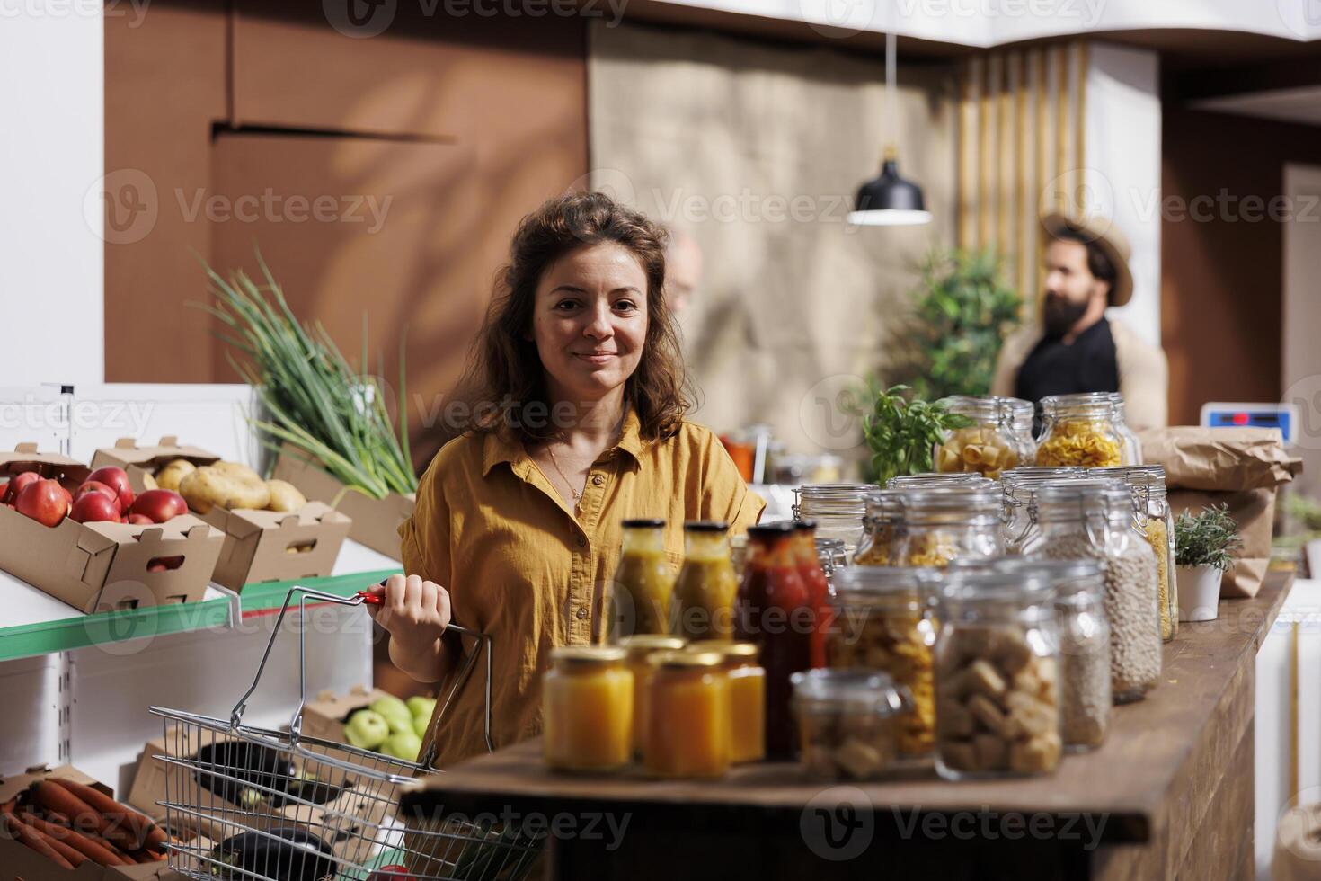 Portrait of smiling woman looking for fresh vegetables in eco friendly zero waste store. Happy customer doing grocery shopping, buying organic bio food items in local neighborhood store photo