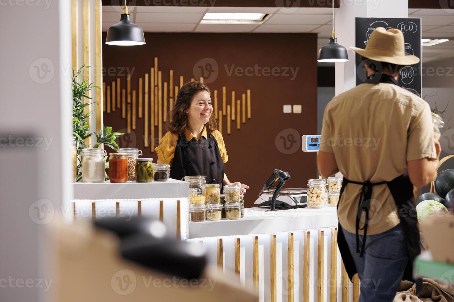 Happy vendor awaiting clients in zero waste store designed to minimize plastic usage, creating positive environmental impact. Cheerful seller and coworker selling ethically sourced pantry staples photo