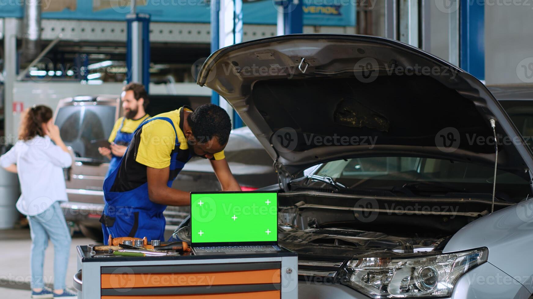 Engineer in car service uses torque wrench to tighten bolts inside vehicle with green screen laptop in front. Expert utilizes professional tools to mend automobile next to chroma key device photo