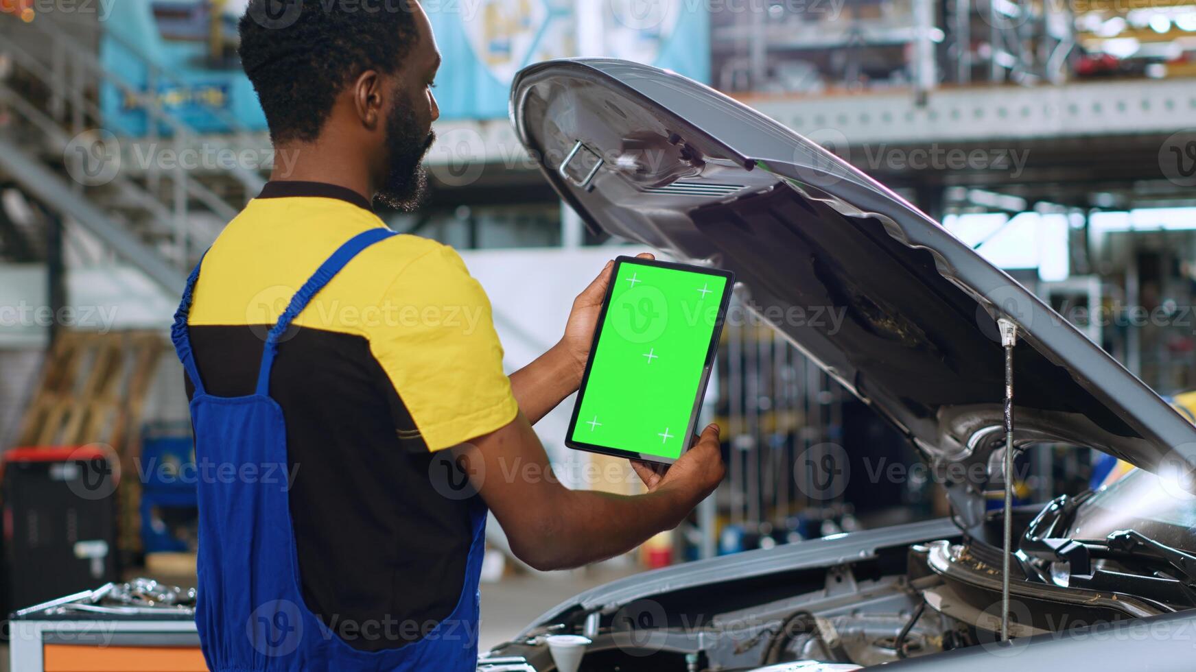 Trained repairman using green screen tablet in car service to order new parts for busted vehicle. Repair shop employee using chroma key device to look online for replacing components photo