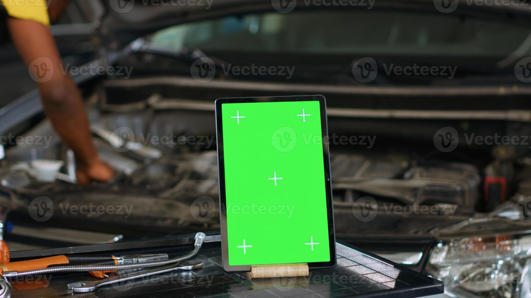 Close up shot of tablet placed on working bench in busy garage next to professional tools while engineer fixes vehicle. Mockup device in repair shop with precise expert working in blurry background photo