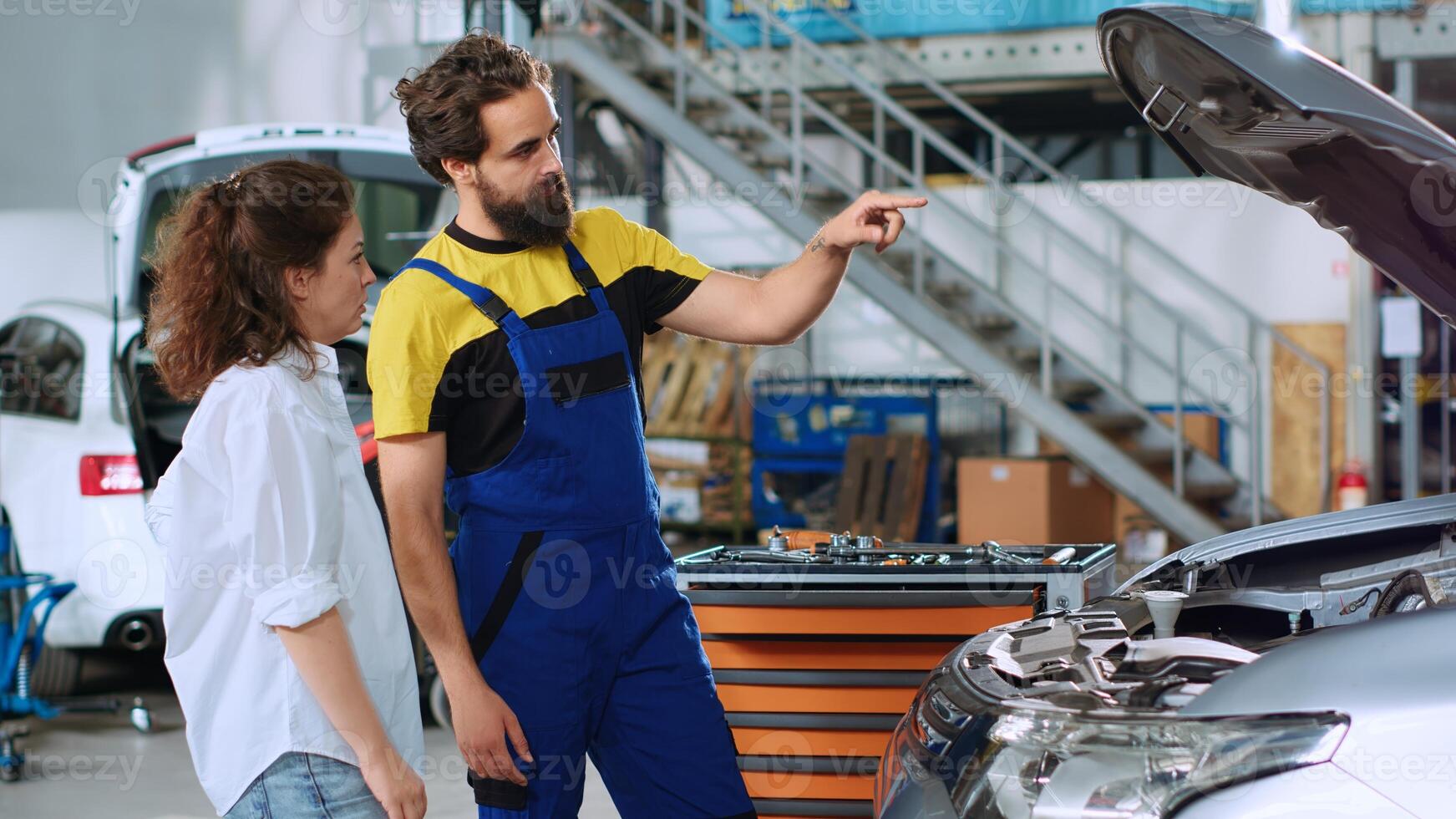 Mechanic in car service using augmented technology hologram to show woman automobile reaction to road conditions after fixing it. Repairman using AR technology with client to test vehicle engine photo