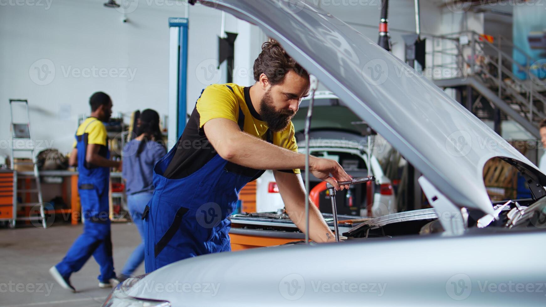 Licensed repairman in car service picks torque wrench from work station bench, using it to tighten bolts after replacing engine. Garage worker uses professional tools to fix client automobile photo