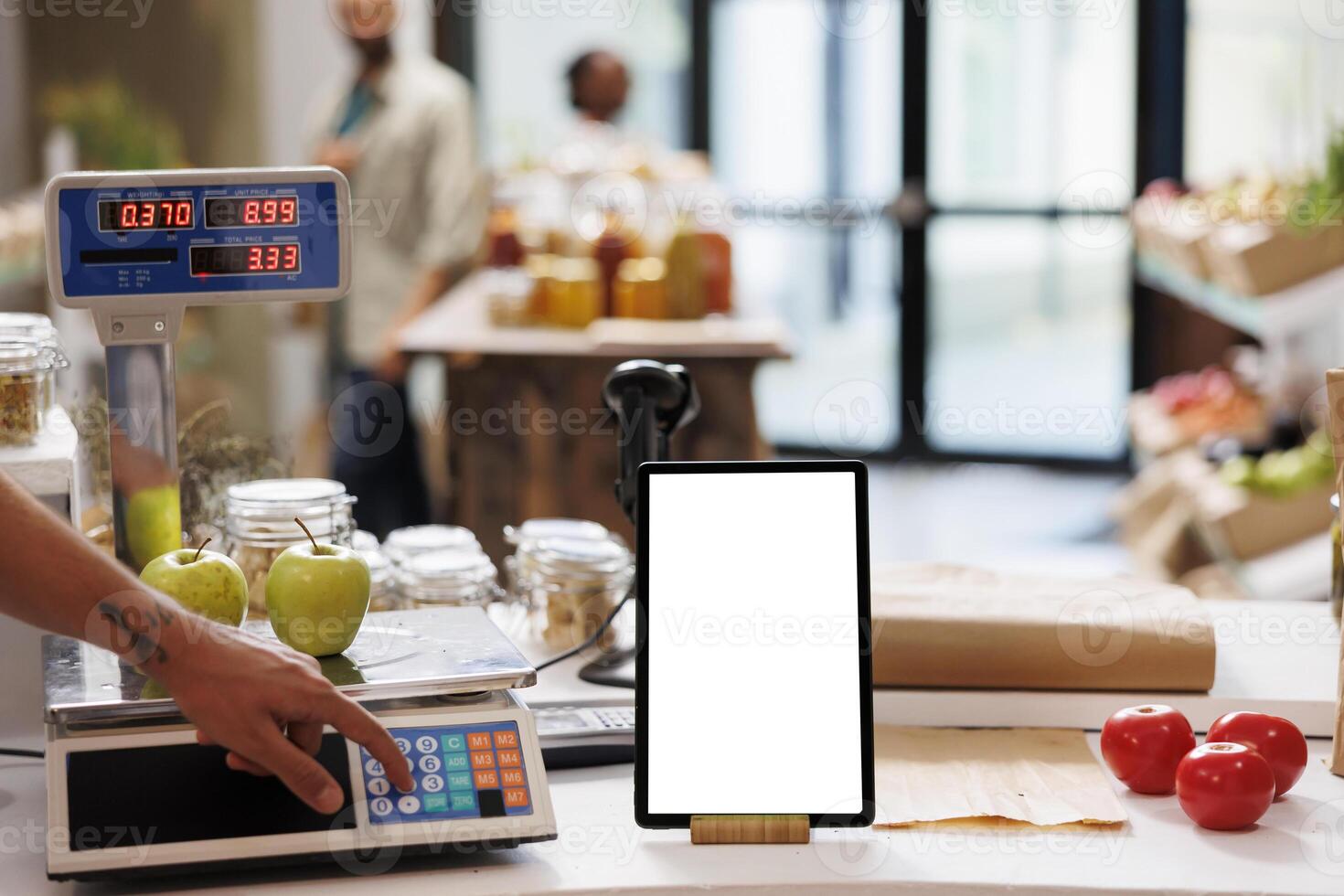 Digital tablet displaying a white screen while salesperson is using an electronic weight scale nearby. Smart device with isolated chromakey template is vertically positioned on checkout counter. photo