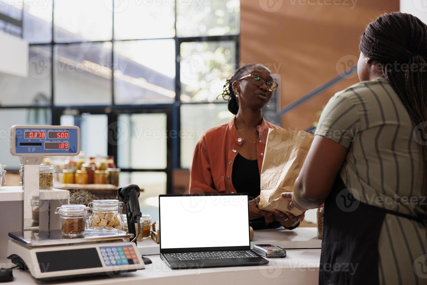 Blank white screen displayed on laptop while black woman with glasses receives her zero waste package. Isolated device with copy space for advertising or promotion of eco friendly bio food store. photo