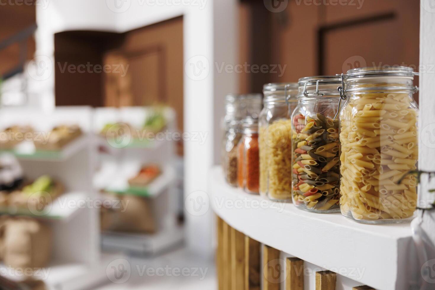 Close up shot of glass containers containing different kinds of pasta put on counter of eco friendly shop. In local supermarket, reusable plastic free jars show various organic bio food ingredients. photo