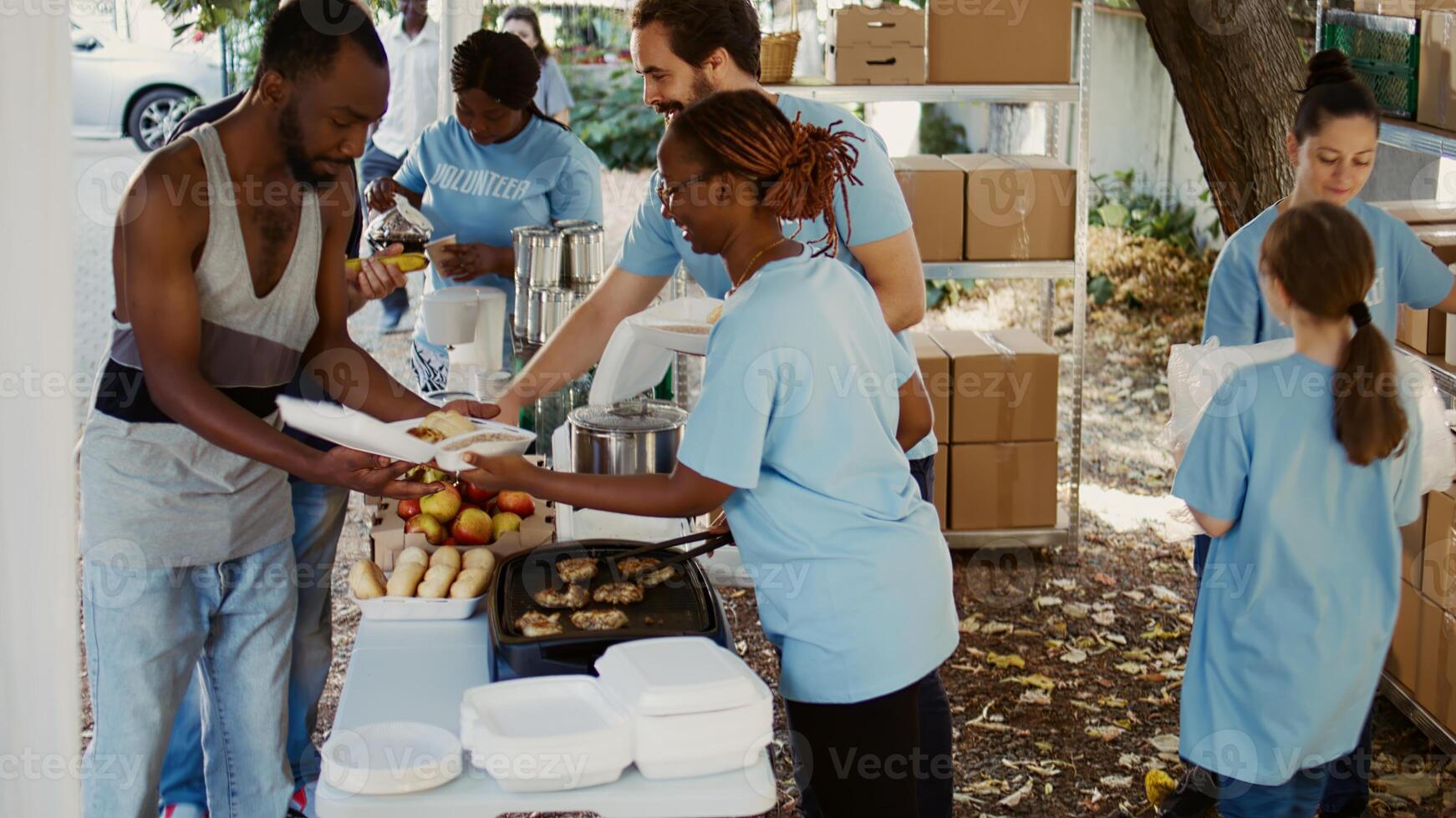 At local center, group of volunteers arranging donation boxes and preparing hot meals for individuals facing hunger and poverty. Youthful charity workers handing out free food to the needy. Handheld. photo