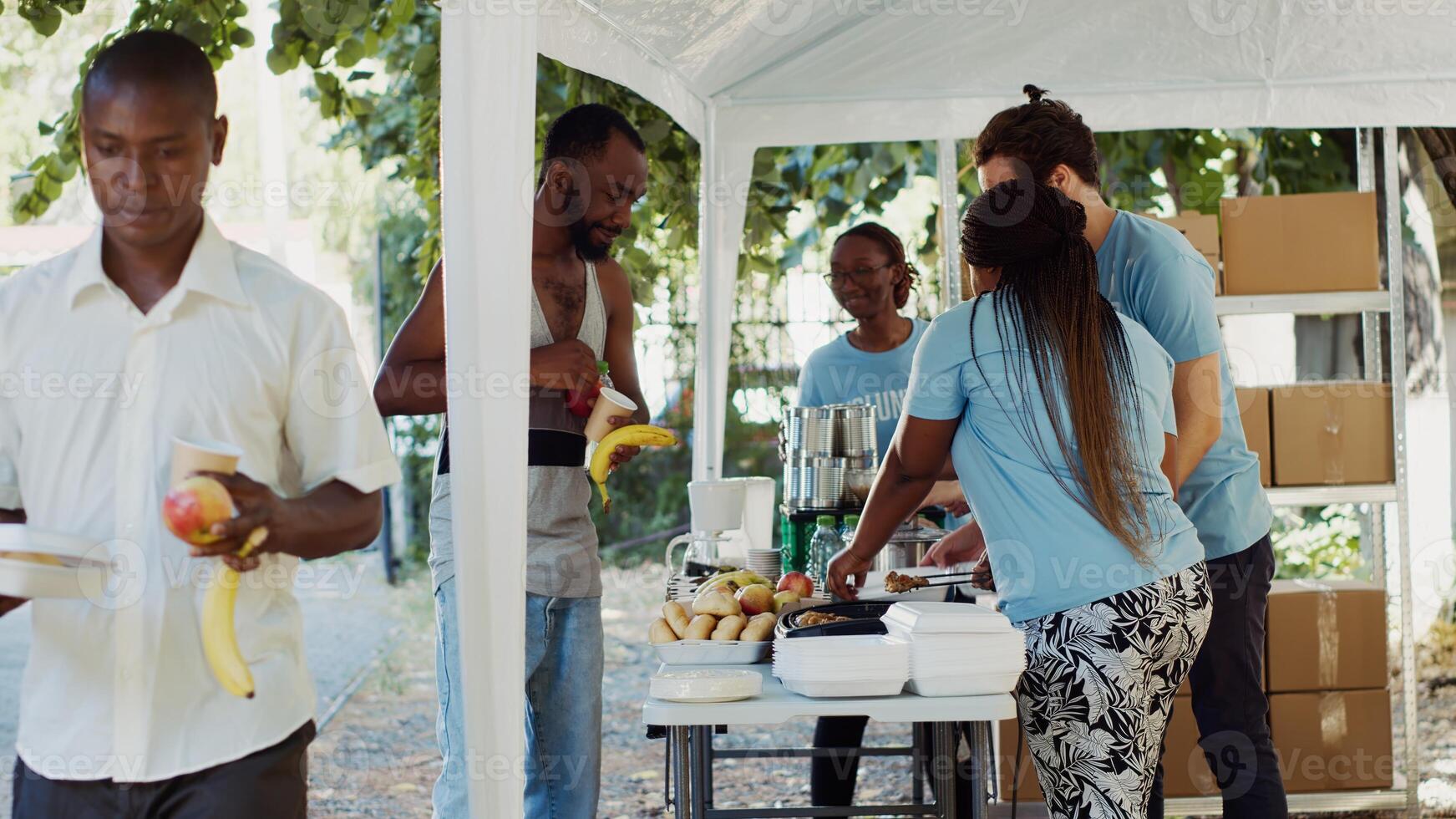 Voluntary individuals at food distribution event generously giving essential supplies to the needy. People of various ethnicities in blue t-shirts offering hunger relief aid through volunteering. photo