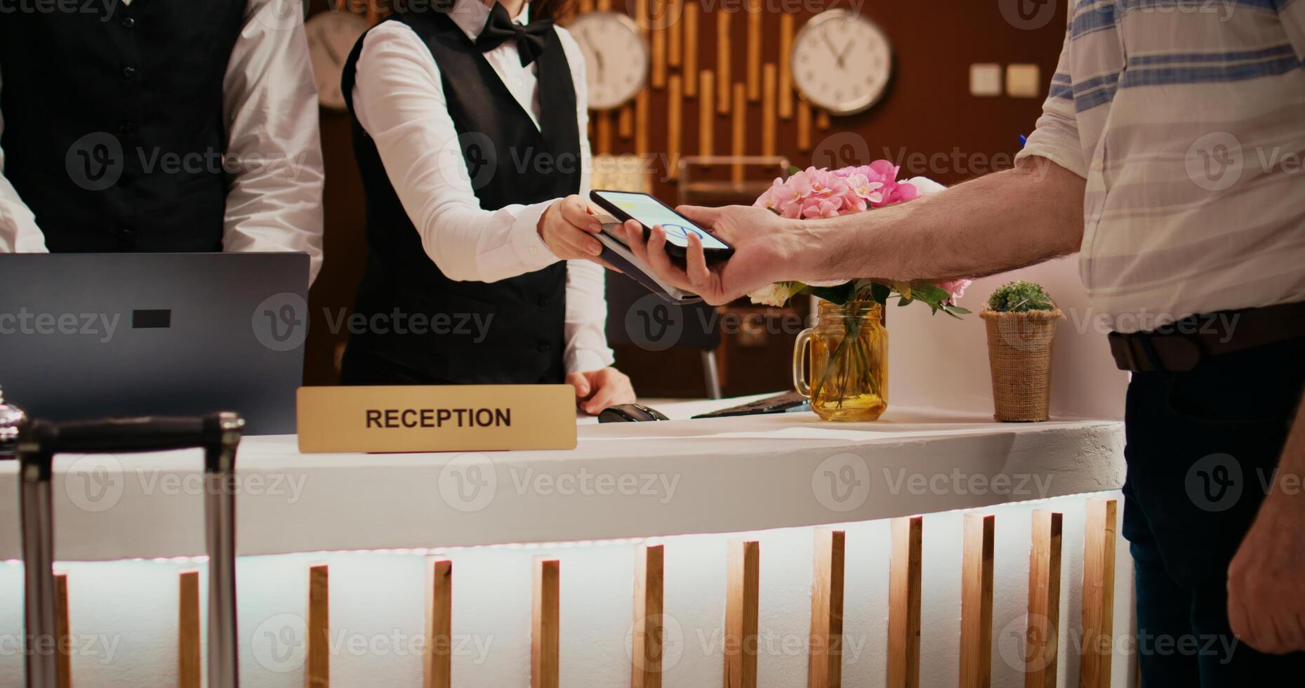 Senior man makes nfc payment with mobile phone at pos terminal, paying for room at five star hotel. Person arriving at reception desk and doing check in for vacation. Close up. Handheld shot. photo