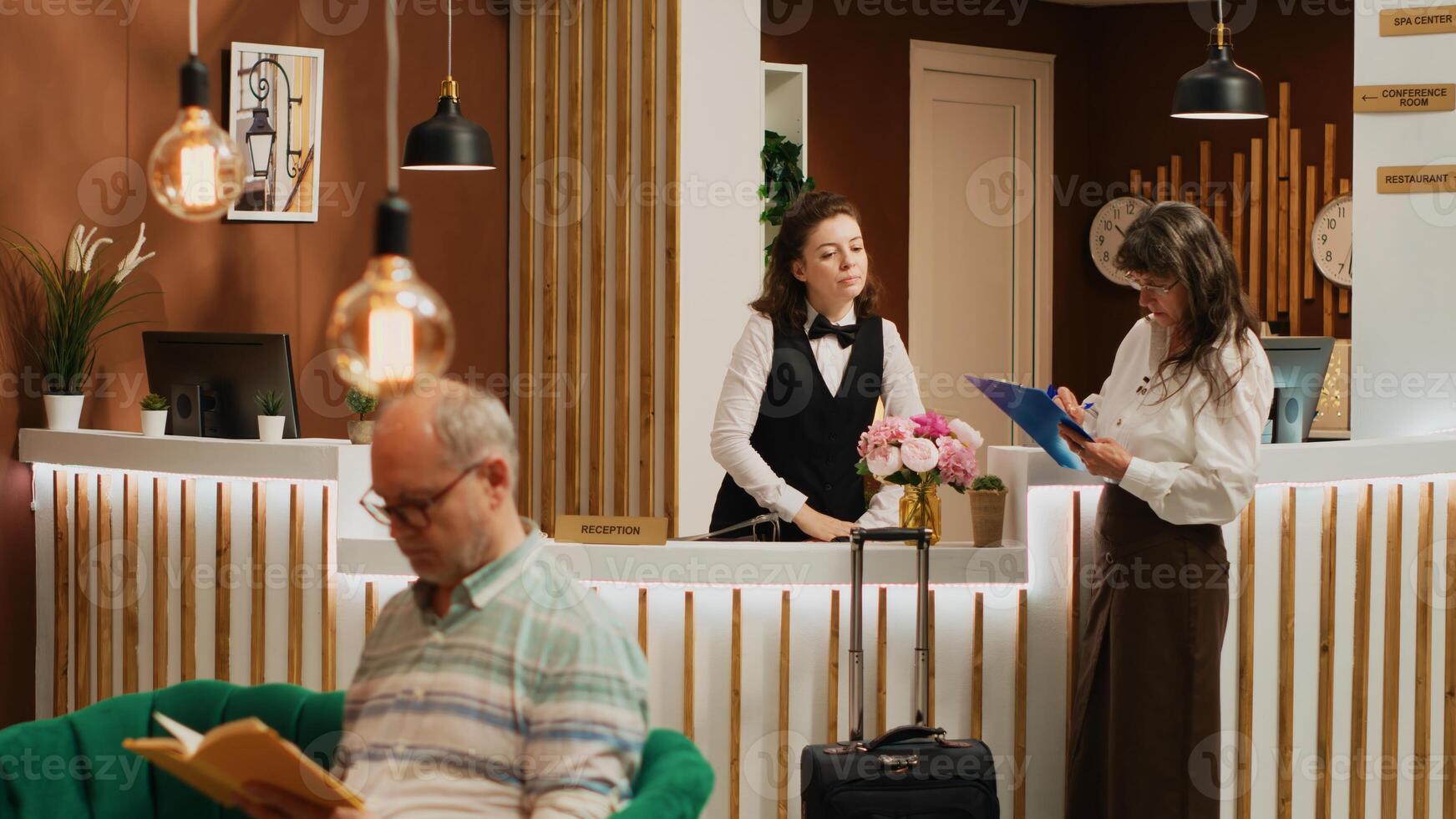 Old person filling in registration forms at front desk, passing check in process and preparing to start retirement holiday trip. Woman with luggage asking receptionist about all inclusive offers. photo
