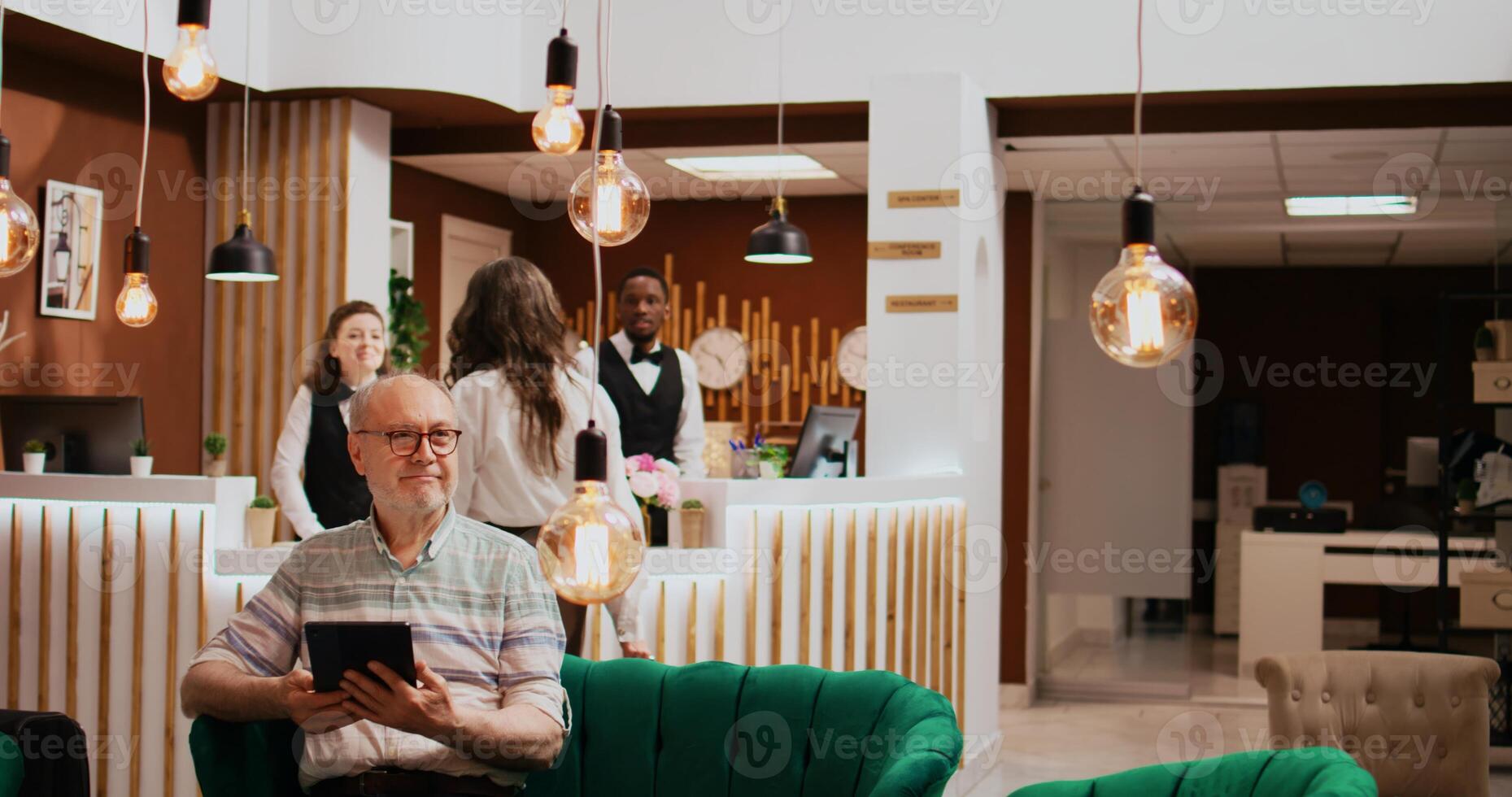 Older man checks tablet connection at hotel, relaxing in lounge area before starting retirement vacation. Browsing online websites to find leisure facilities and relaxing activities. photo