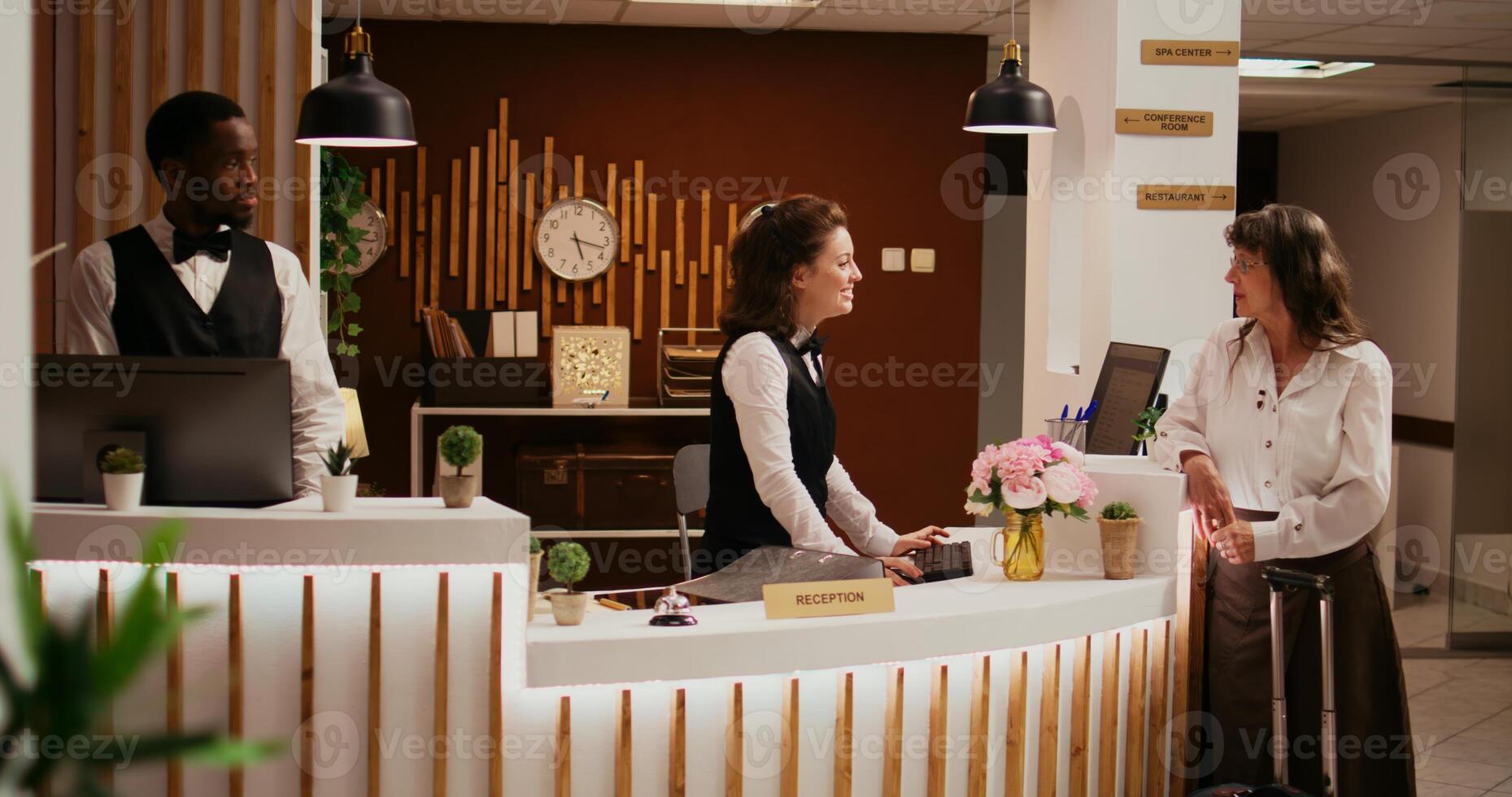Elderly person arriving in hotel lobby, asking concierge about senior travel offers for wellness and leisure activities. Employee welcoming tourist at reception, ensuring relaxing stay. photo