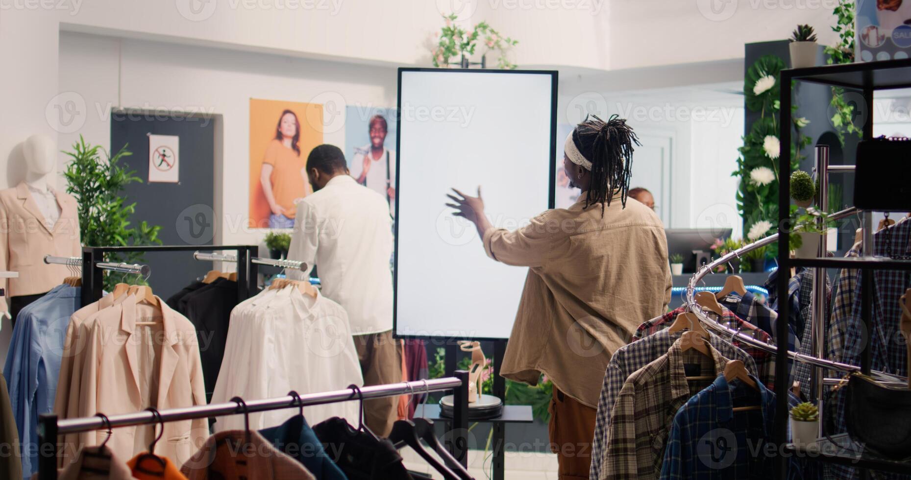 Man in shopping center fashion boutique using high tech screen to look at clothes options to try on. Client using led panel to visualize outfit combinations in store before buying, ground level shot photo