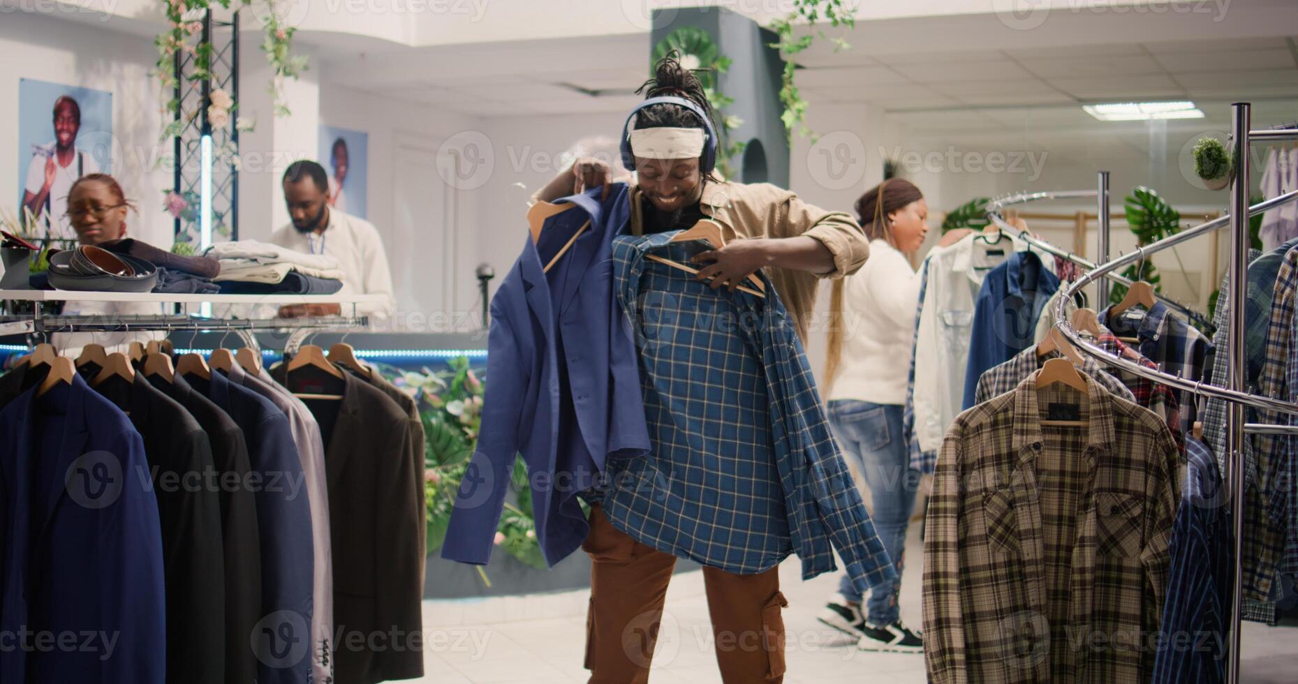 Man listening to music and dancing while looking at elegant clothes in clothing store, trying to determine if materials are qualitative. Client having fun fashion boutique while analyzing garments photo