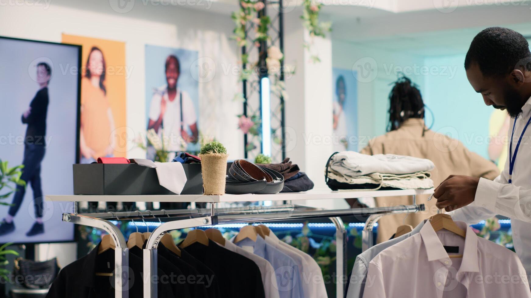 African american employee working in SH clothing shop, placing simple stylish shirts on racks. Retail assistant formal garments merchandise on hangers in discount fashion store photo