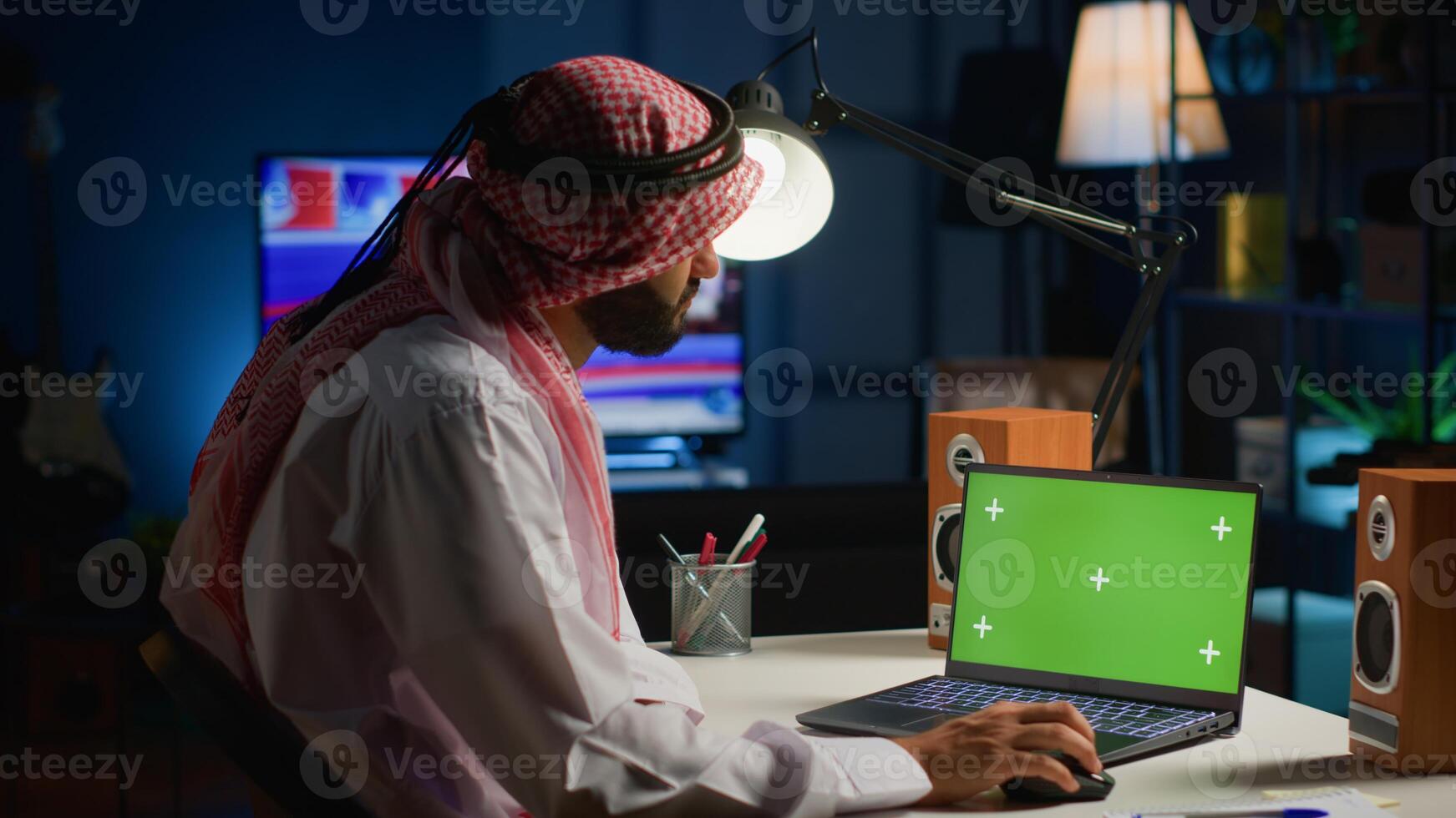 Arab man browsing on mockup laptop while working from home. Self employed freelancer checking emails on isolated screen device in apartment office with TV as background noise photo