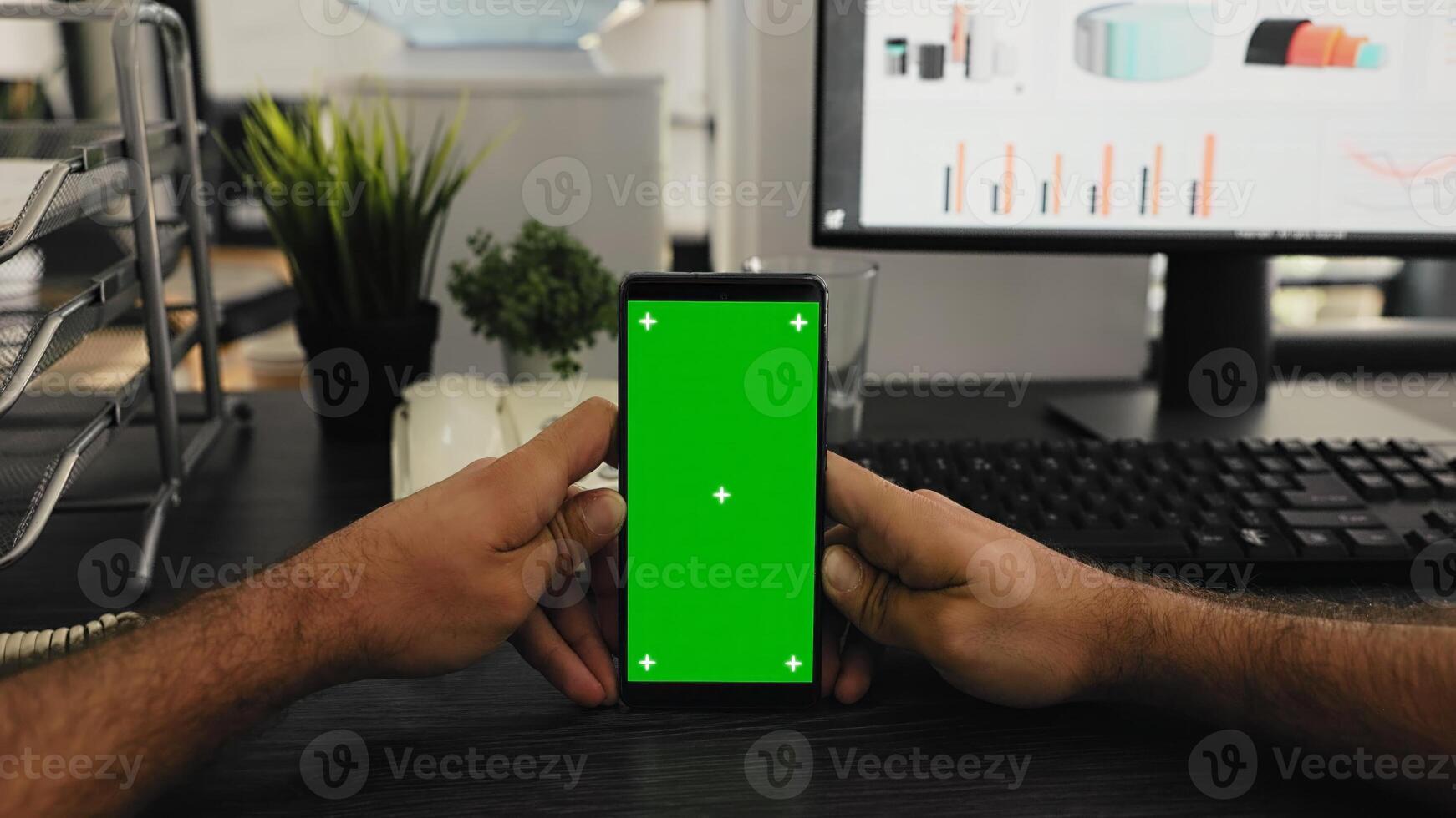 POV of manager holds smartphone with isolated greenscreen layout, working with blank mockup chromakey template at office desk. Young man looking at mobile device display with copyspace. photo