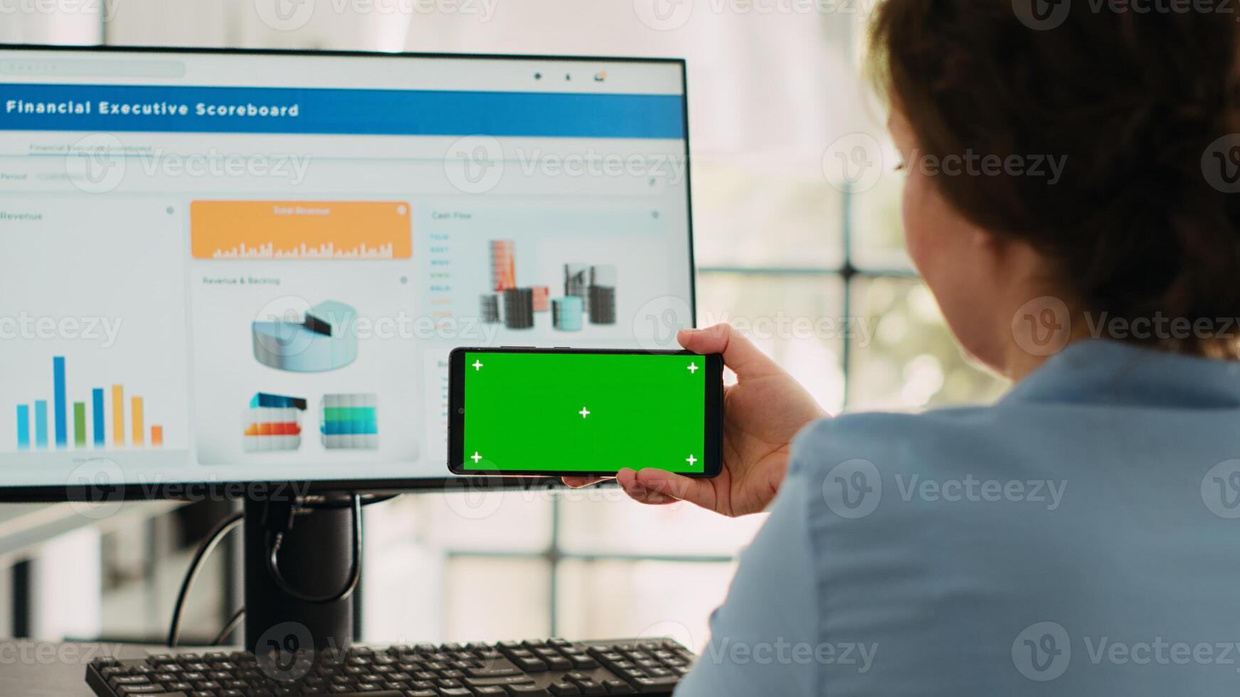 Business specialist shows greenscreen on smartphone software display, looking at isolated chromakey template and working on computer at desk. Using blank mockup and finishing agency operations. photo
