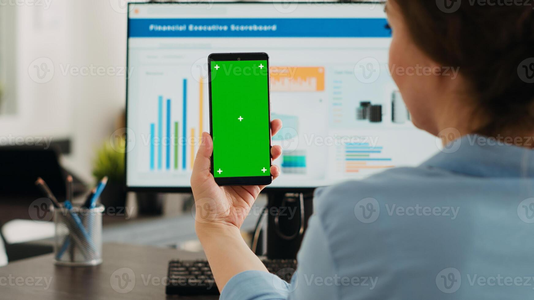 Businesswoman showing greenscreen display in coworking space, holding device with isolated copyspace layout on screen. Person using smartphone with mockup chromakey template. photo