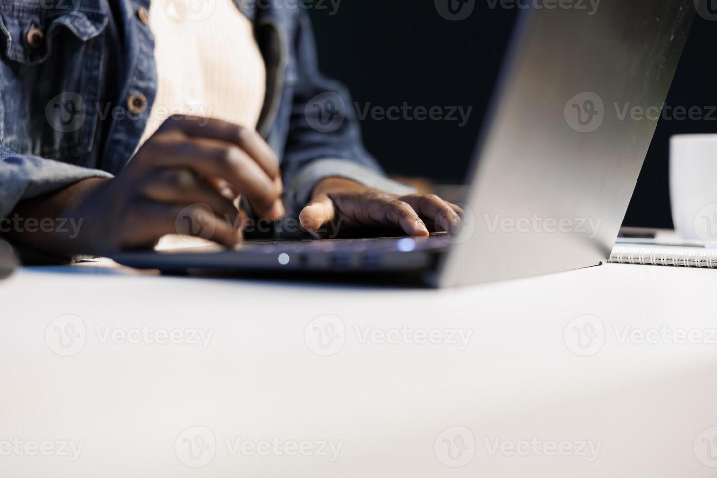 Close up of black person utilizing modern technology by typing on portable computer. Selective focus on hands of african american individual taking notes on laptop and surfing the net. photo