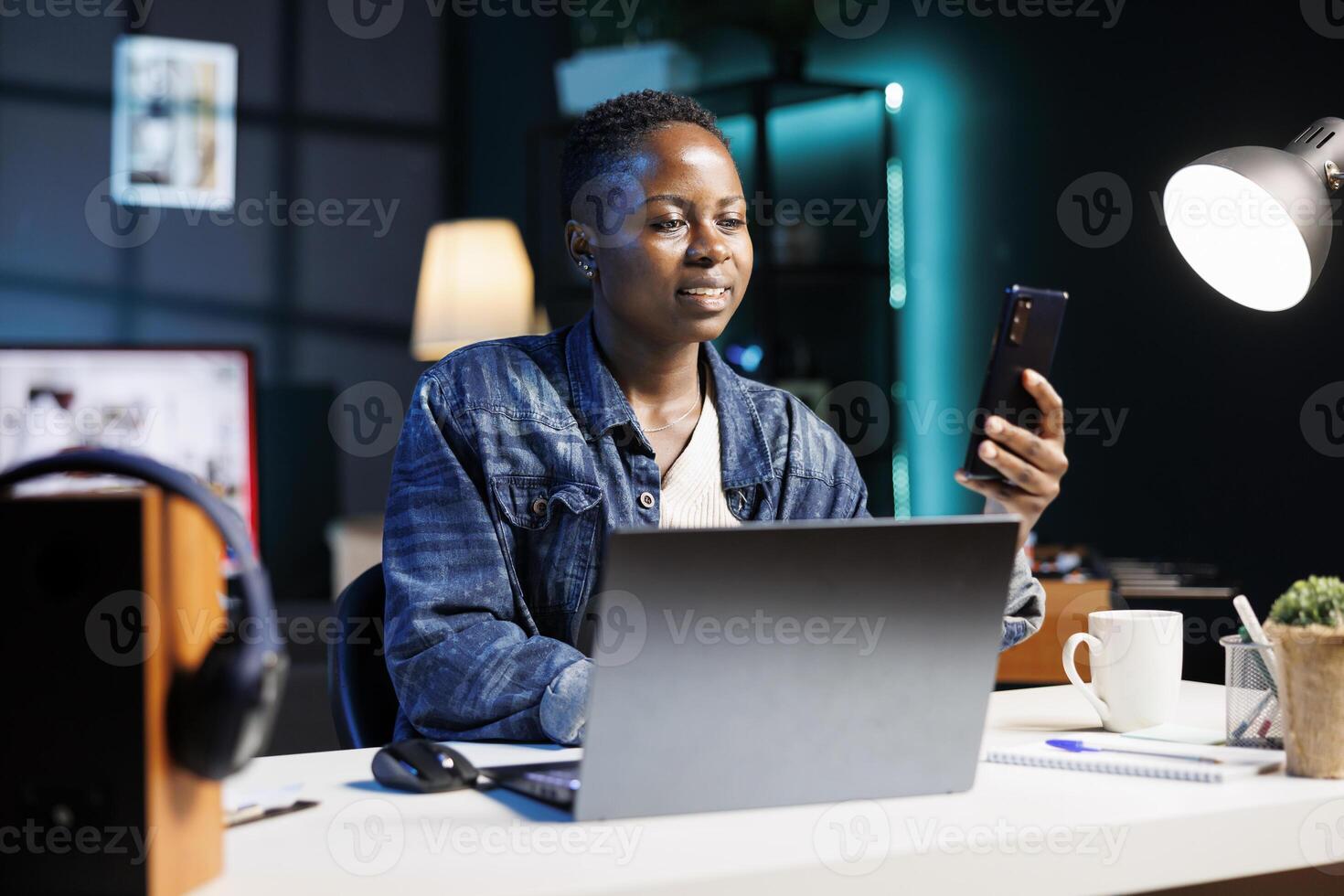 African american female blogger multitasking, using her mobile device and laptop to check her website. Black woman grasping and browsing through the internet, checking email on her smartphone. photo
