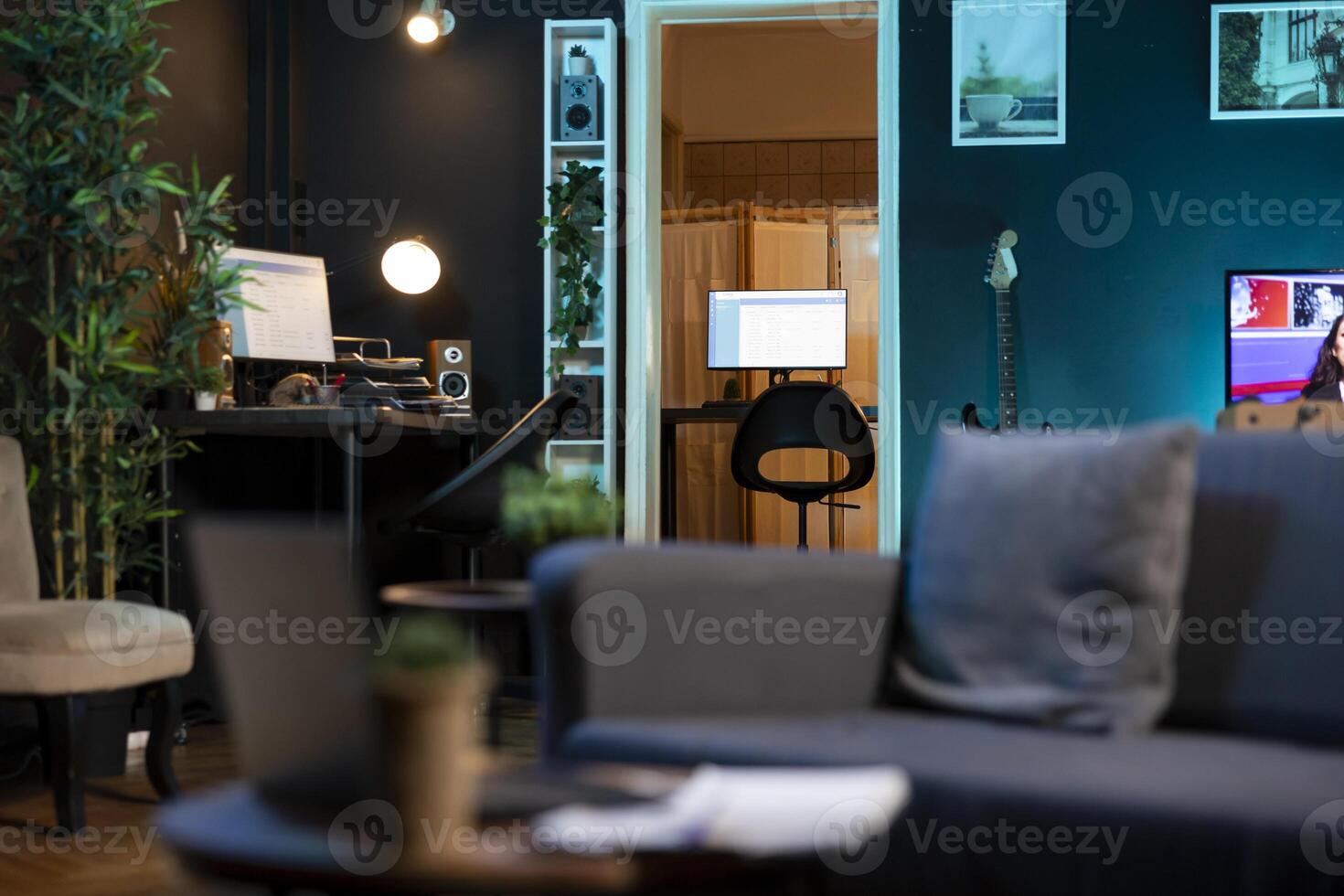 Stylish empty apartment with artwork on walls and computer screen left open at night showing software interface. Home living room with no people in, cozy couch and TV left open photo