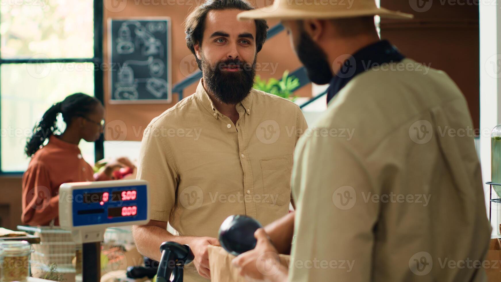 Shop owner serving man with produce after weighting fruits and veggies on scale, putting organic eco products in recyclable paper bag. Client supporting sustainable lifestyle and small business. photo