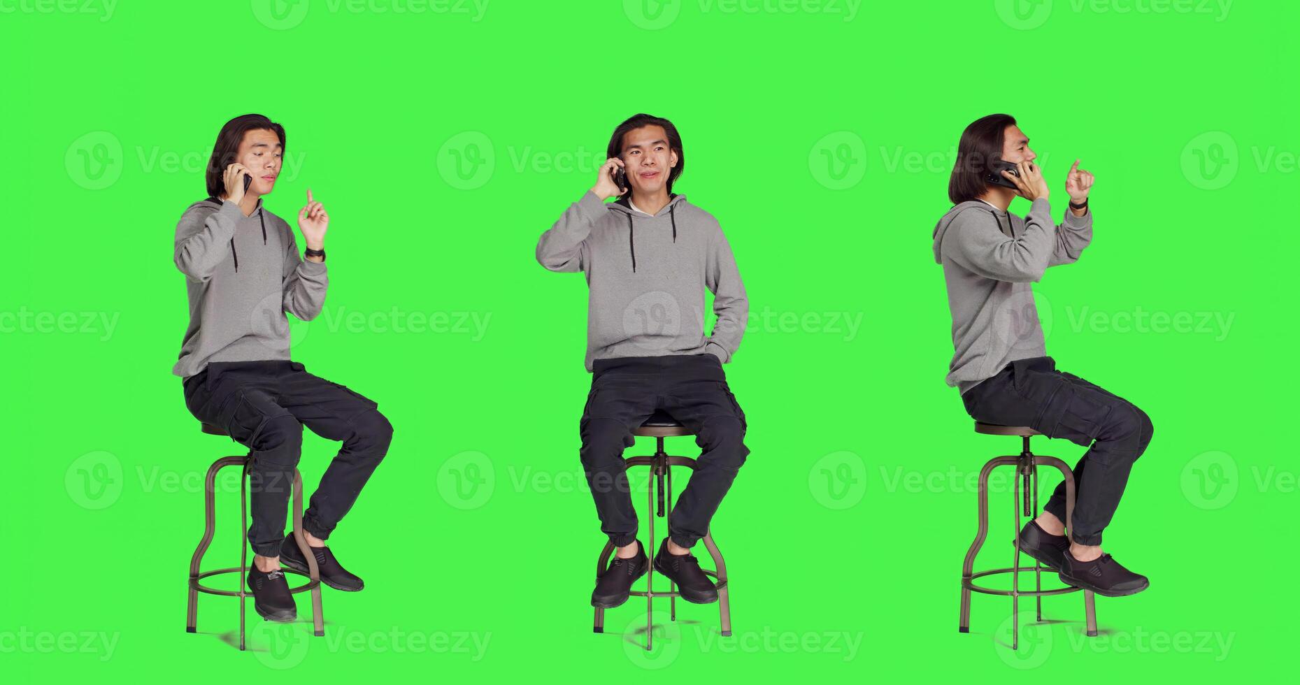 Asian guy texting and answering call on greenscreen backdrop, sending messages on social media using modern phone app. Young adult sitting on chair, calling family and messaging. photo