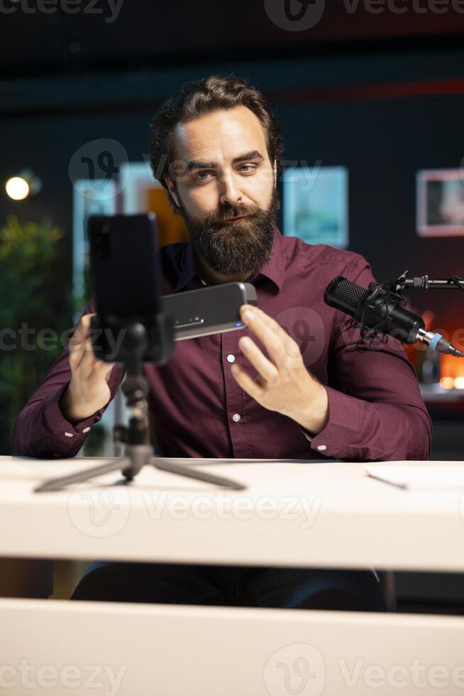 Influencer doing technology review of wireless portable speaker for internet platforms channel, filming with mobile phone. Influencer showing to music playing device, recording with smartphone photo