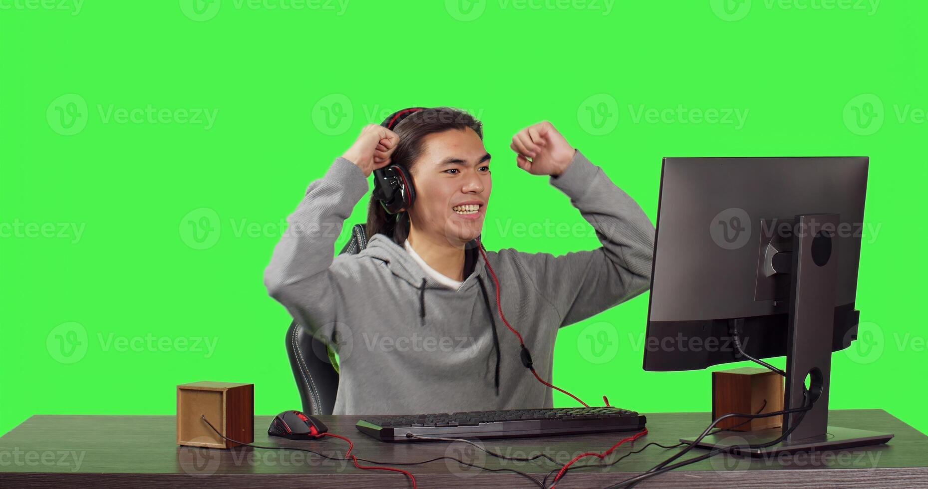 Asian adult being on pc at workstation, playing online rpg games with his friends. Young man having fun with new web contest, talking to people on headset over greenscreen backdrop. photo