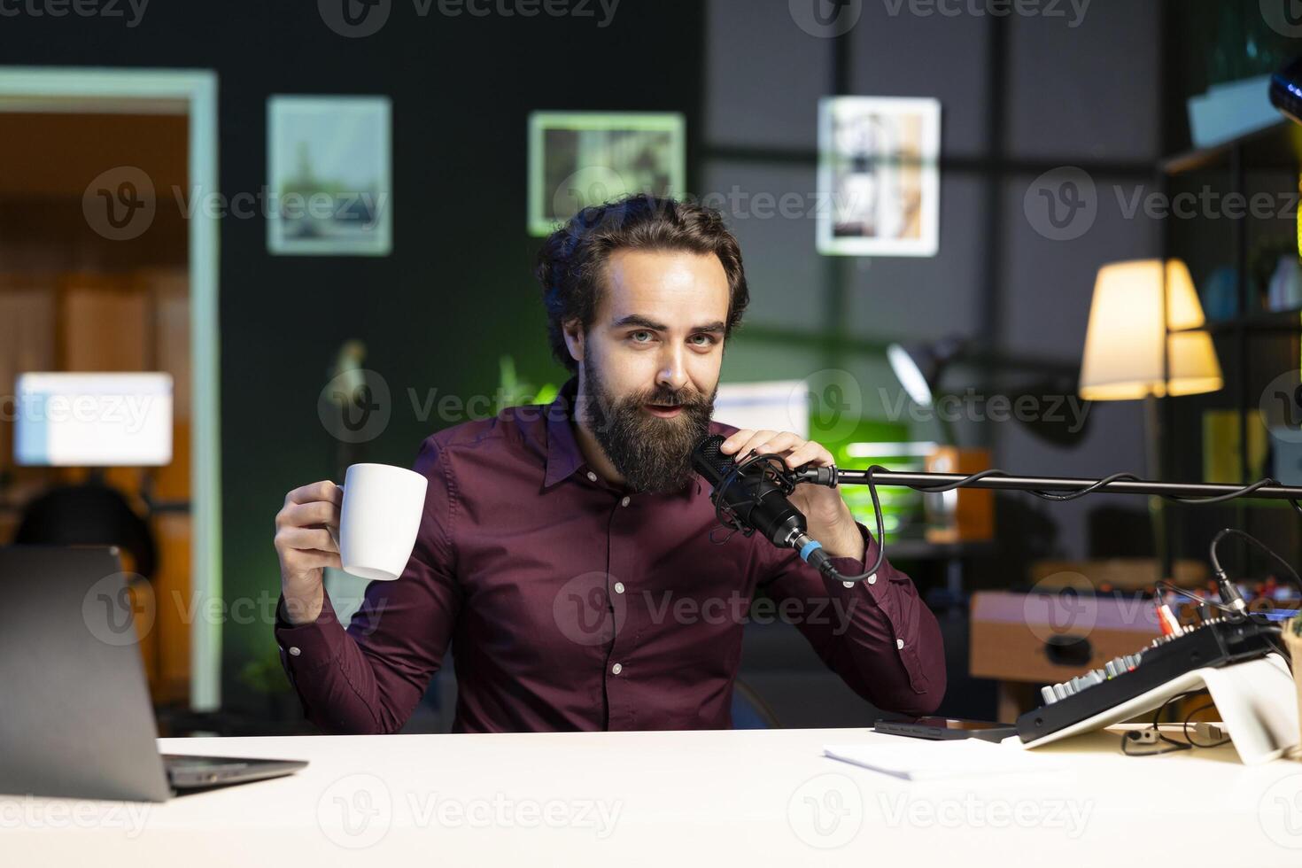 Media star talking in professional microphone in studio at night and drinking coffee, filming internet production. Content creator uses quality mic to speak to audience, enjoying hot beverage photo
