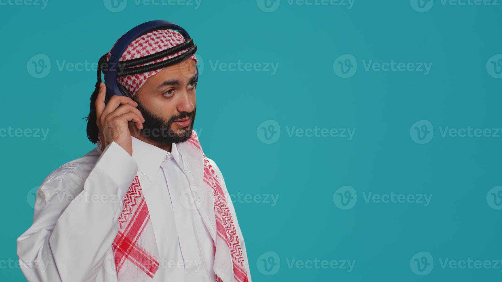 Groovy adult dancing around on camera, listening to funky songs on audio headset and having fun in studio. Middle eastern person in traditional islamic attire showing fun dance moves. photo