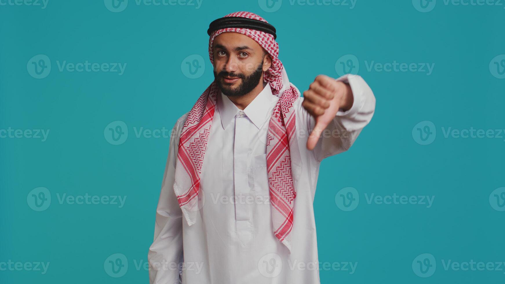 Islamic adult gives thumbs down and feeling disappointed about something, indicating muslim culture with traditional robe and scarf. Young person presenting rejection and negative sign. photo