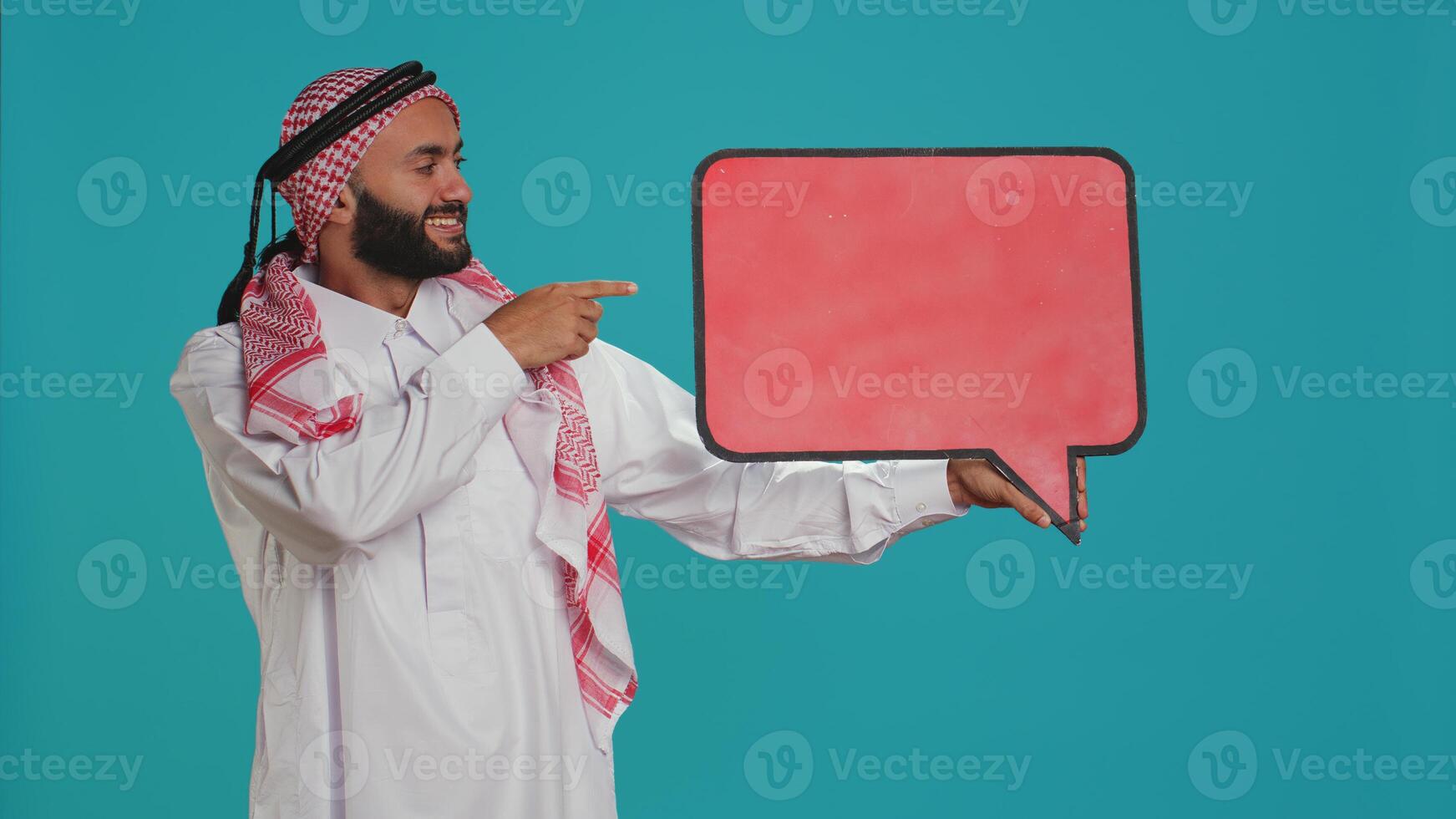 Muslim man shows speech bubble on camera, creating advertisement for new web commercial. Young guy working in marketing industry with isolated cardboard sign, empty billboard. photo