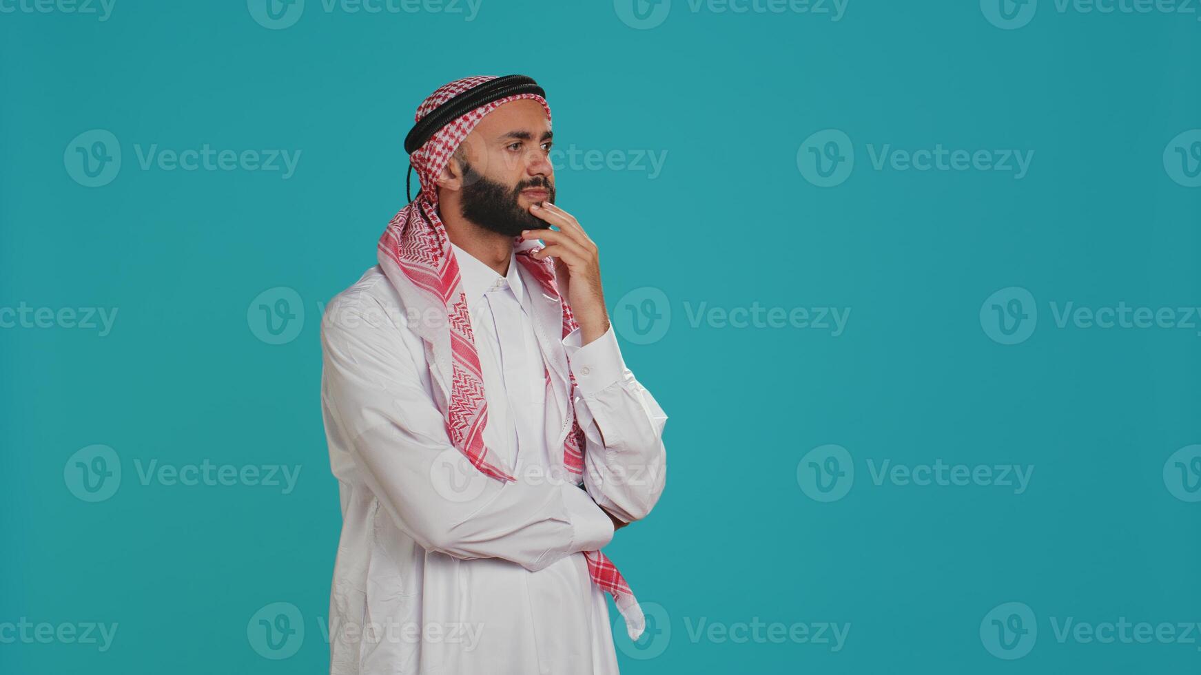 Muslim person looks contemplative and thinking about innovative solutions, acting interested and trying to find answer. Young guy with headscarf being thoughtful and puzzled on camera. photo