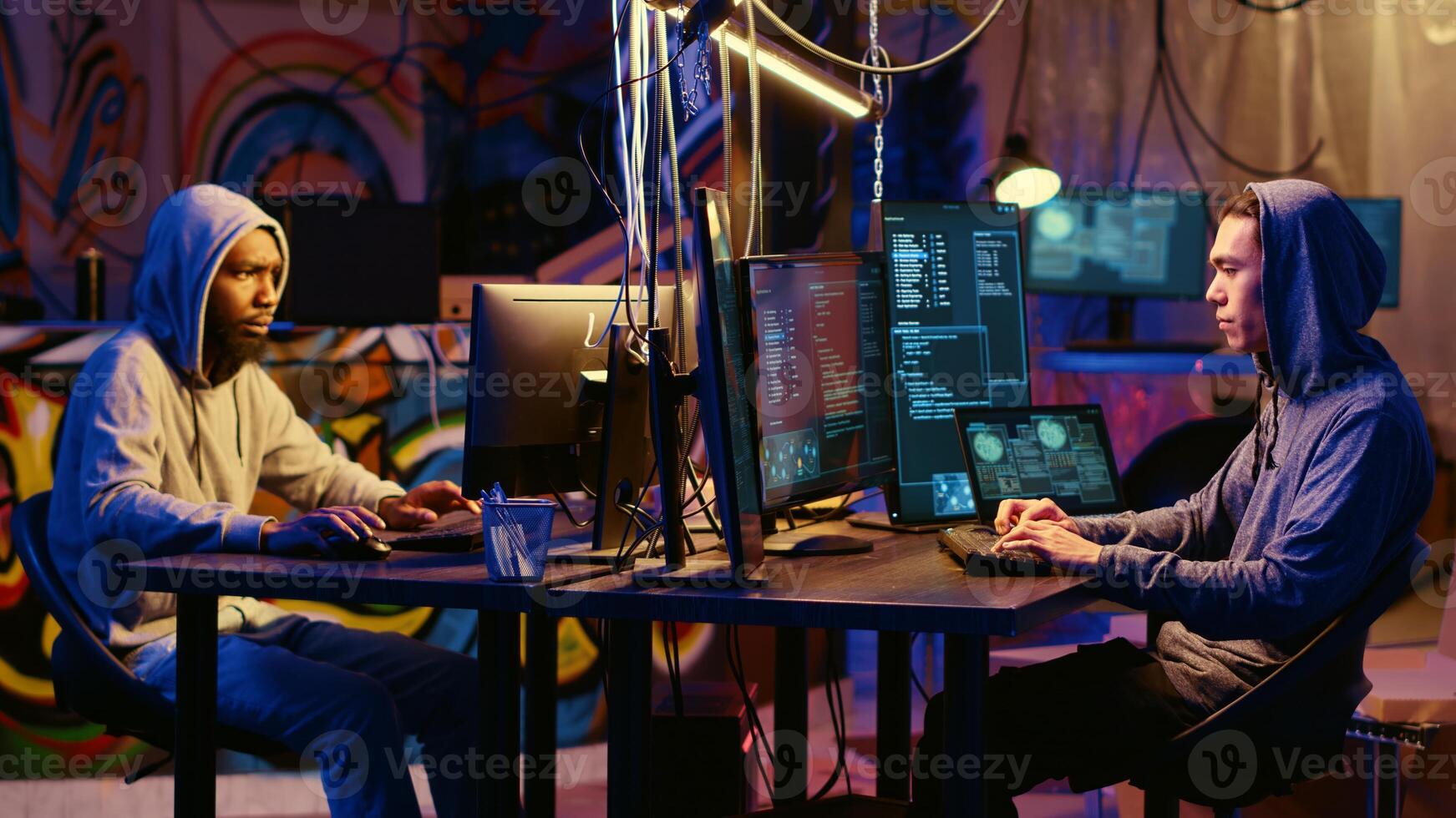 Hacker group members working together in hidden place with graffiti walls, deploying malware on unsecured computers to steal sensitive and private information from internet users photo