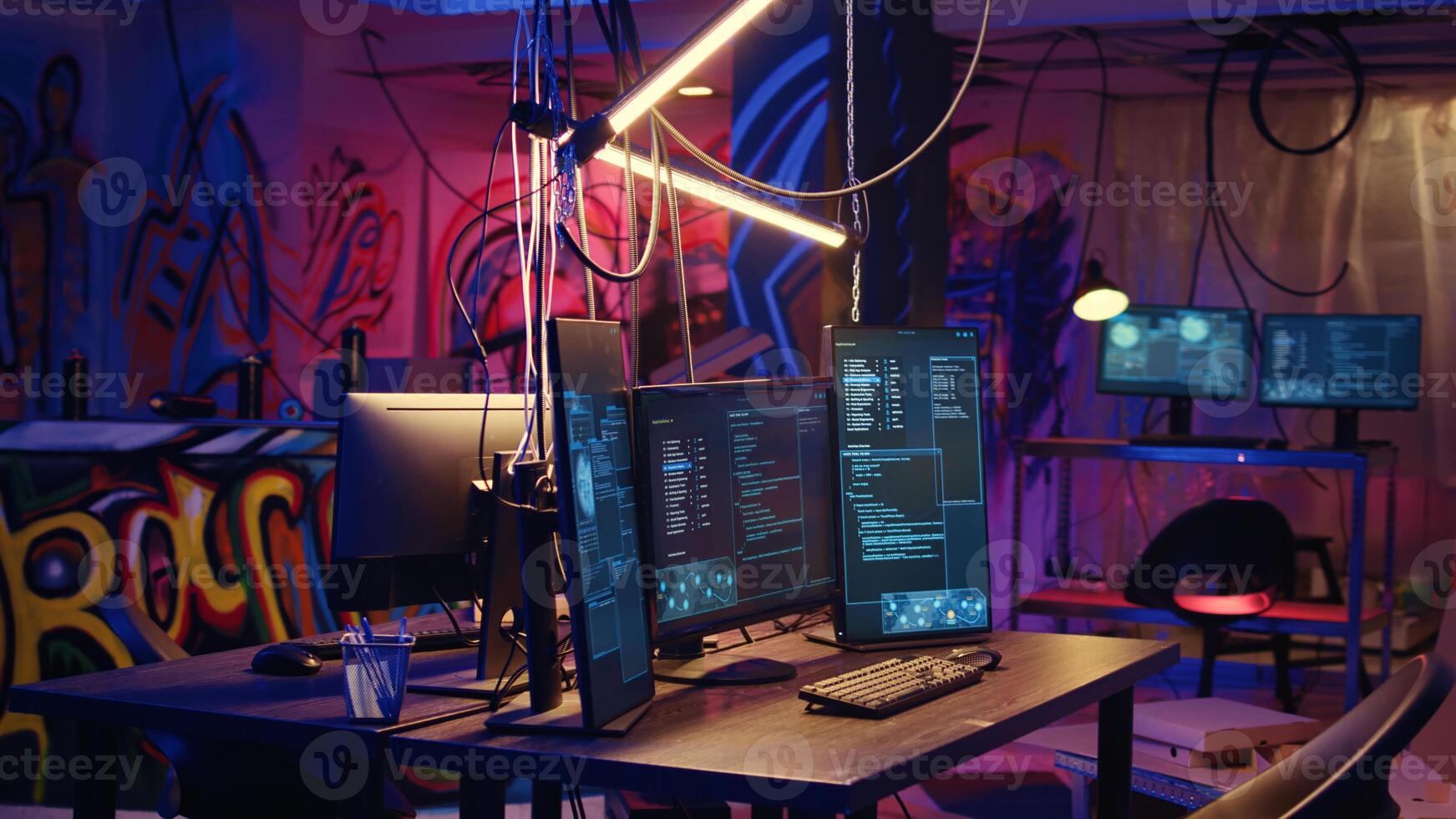 Panning shot of high tech computer system running malicious code in empty basement. PC monitors in empty neon lit criminal hideout used by hackers to commit illegal activities photo