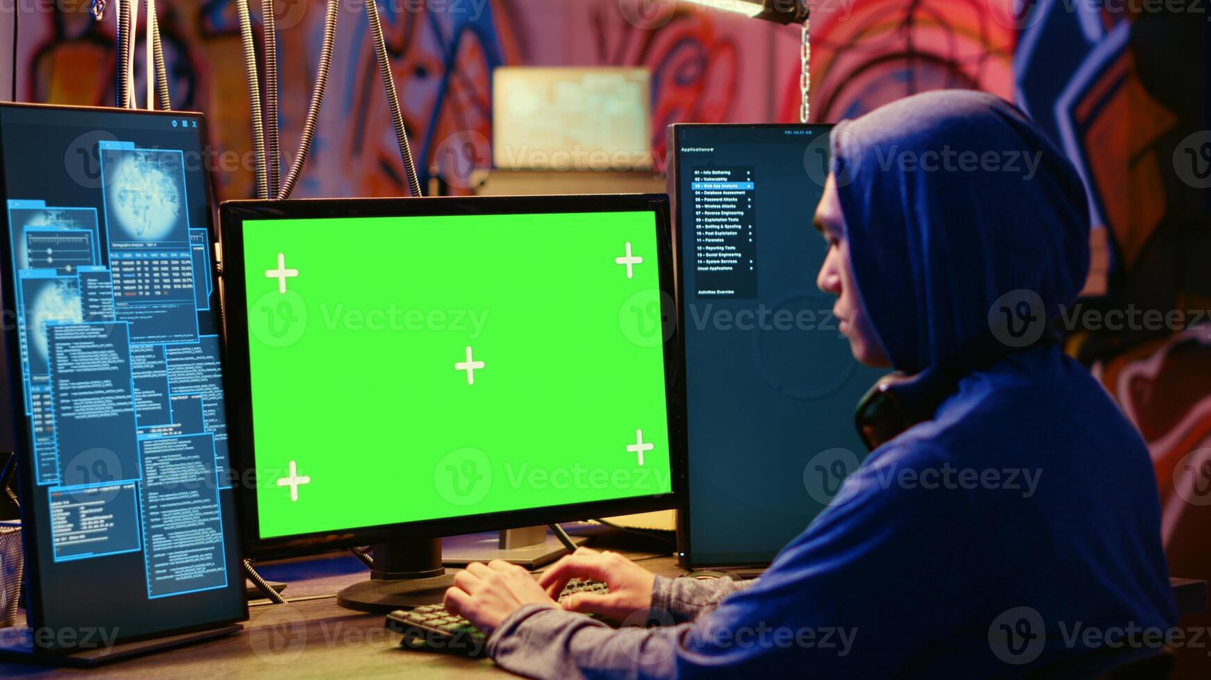 Asian hacker in hidden place with graffiti walls using green screen computer to deploy malware on unsecured devices, stealing sensitive data from unaware users online and selling it on black market photo