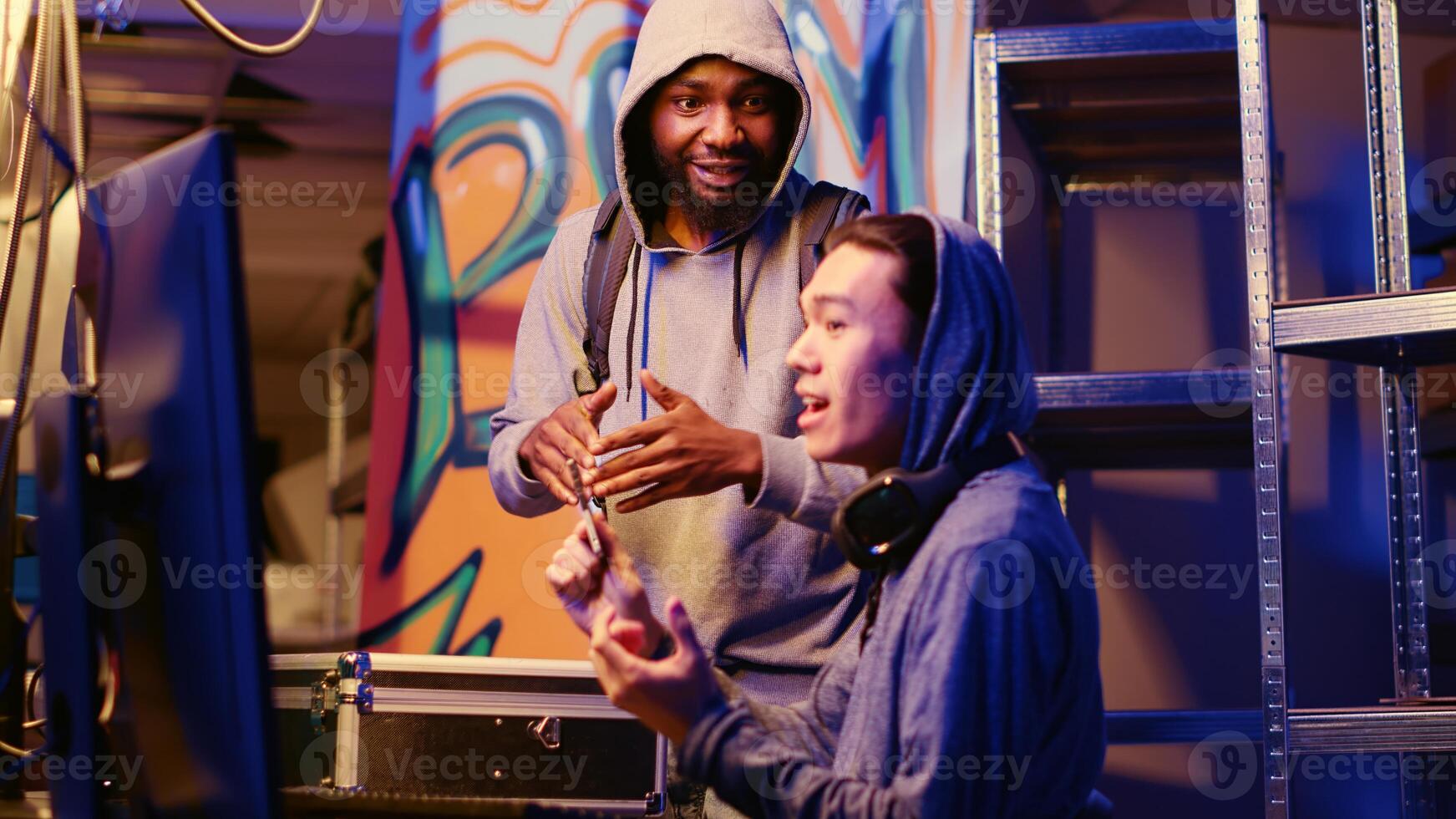 Hacker arriving in hidden warehouse headquarters with SSD containing sensitive data obtained from victim through ransomware virus, celebrating with colleague after completing evil plan photo